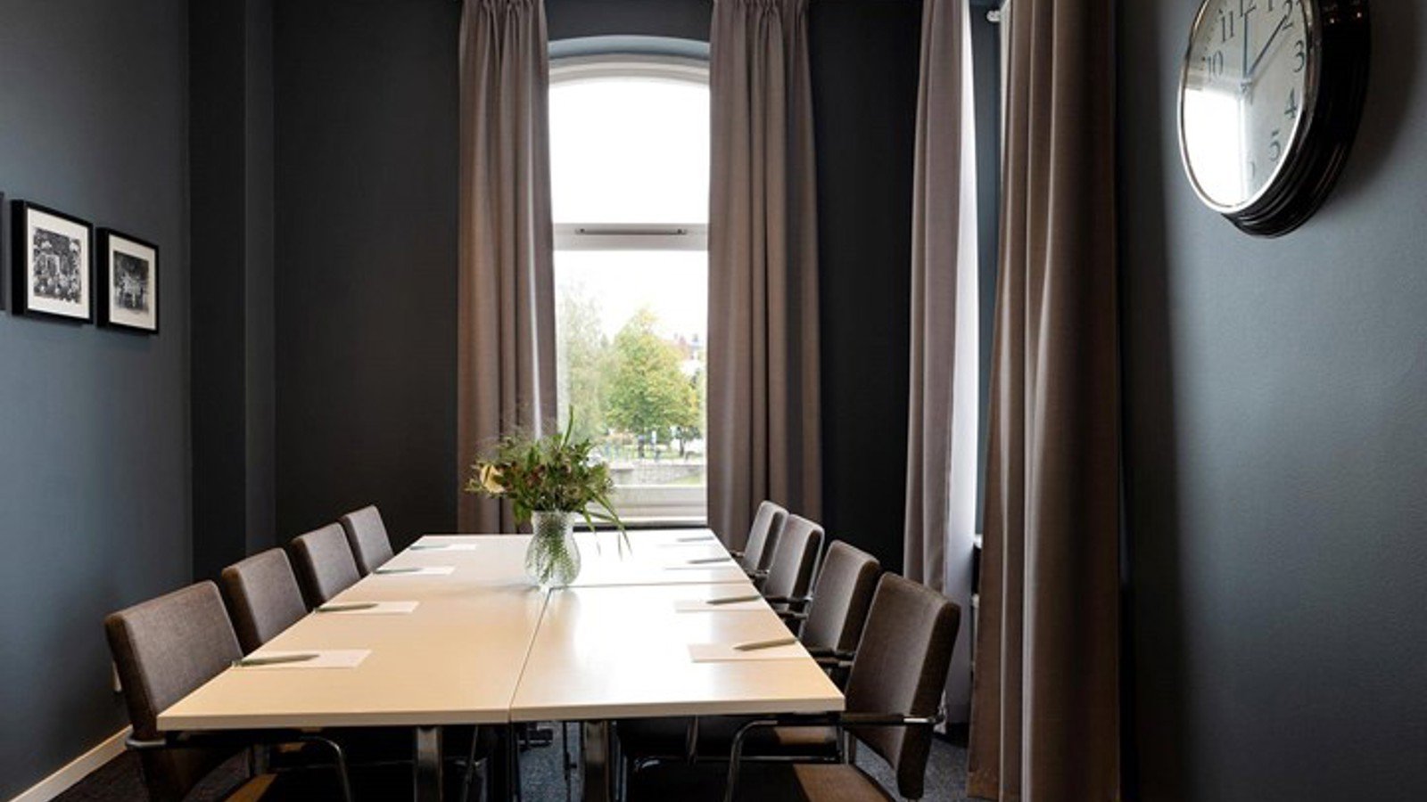 Boardroom with large windows, dark walls, white table with flower vase