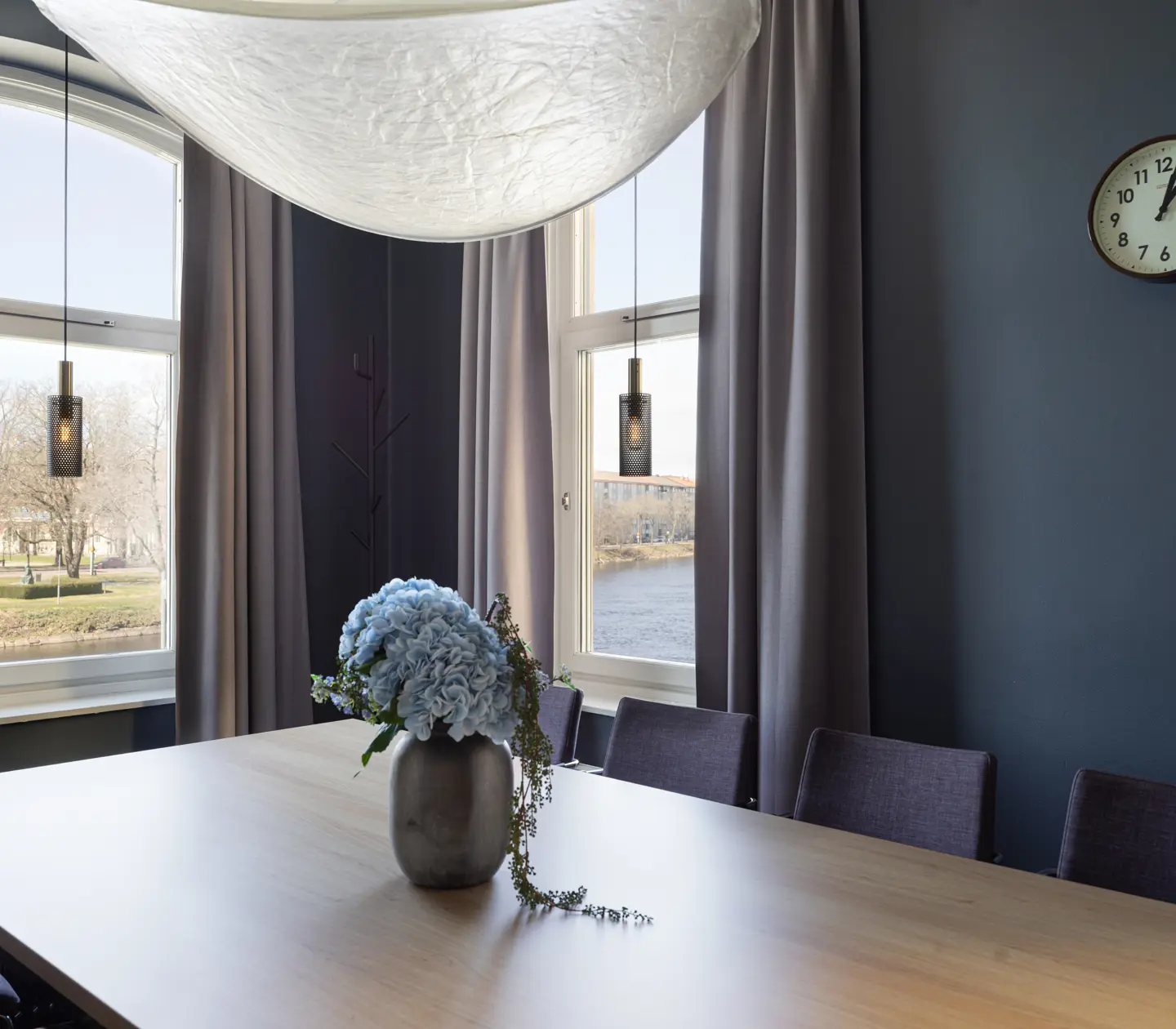 Modernt mötesrum med ljusinsläpp, blå väggar, böjd lampa, klocka och blombukett på bordet.