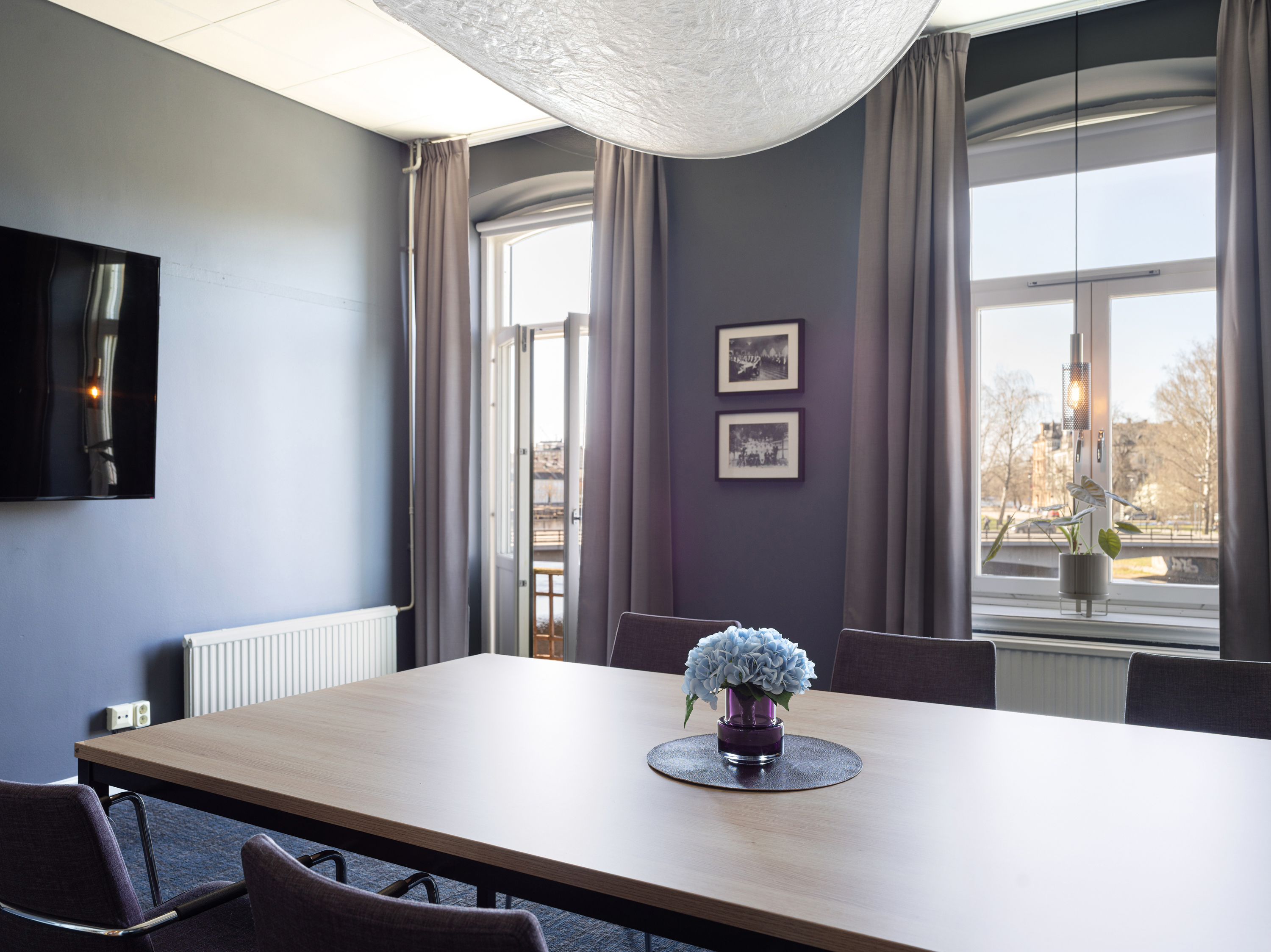 Modern conference room with blue walls, large window, and a wooden table adorned with a vase of blue flowers.