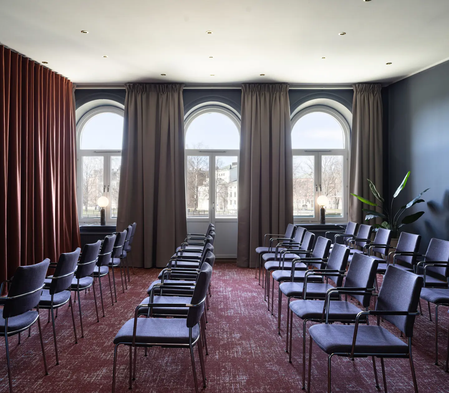 Konferensrum med stolar ordnade i rader, stora fönster med gardiner och röd matta, modernt och ljust inrett.