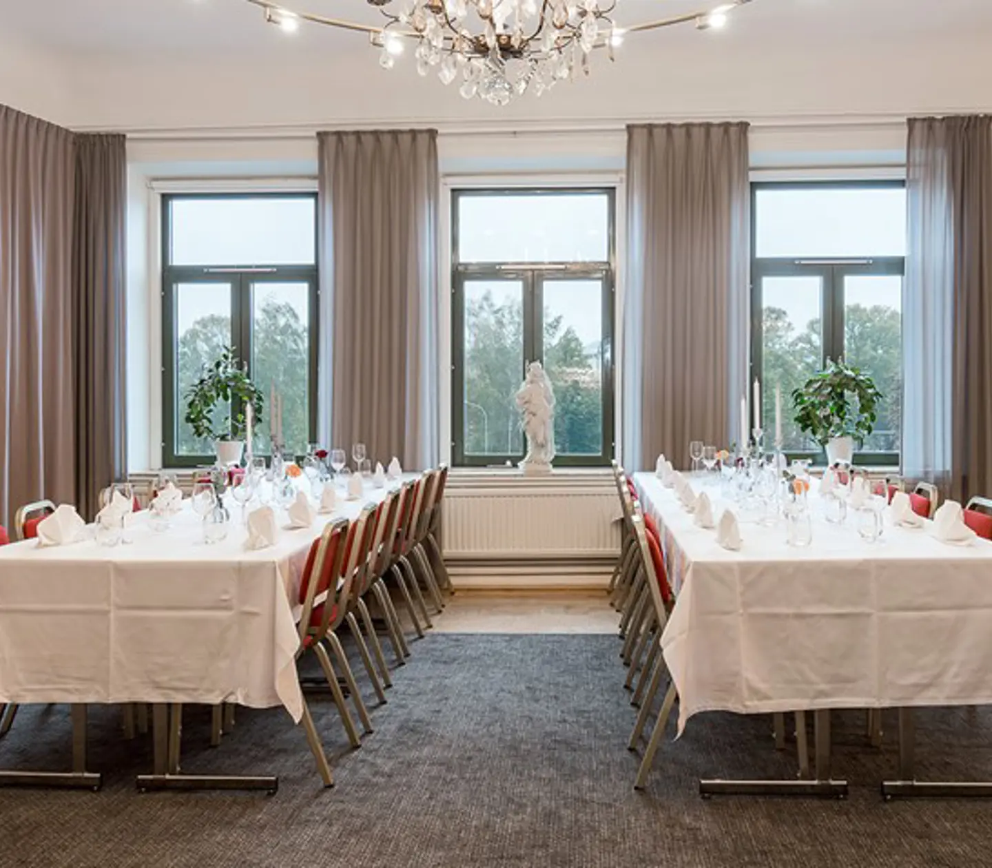 Festlokal med dukade långbord, stora fönster och draperier