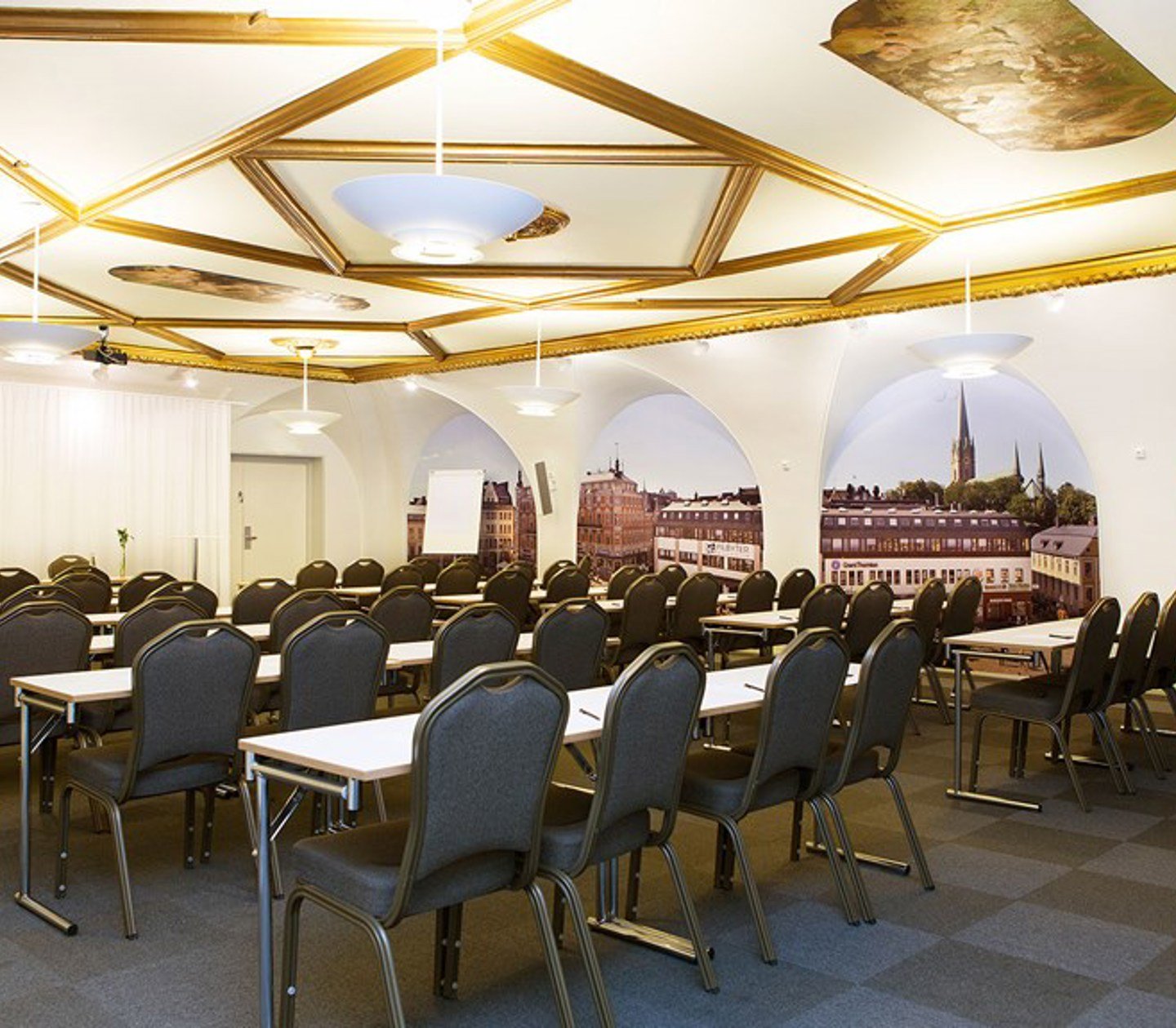Stort konferensrum med skolsittning, upplyst tak med gulddetaljer och mörkt golv