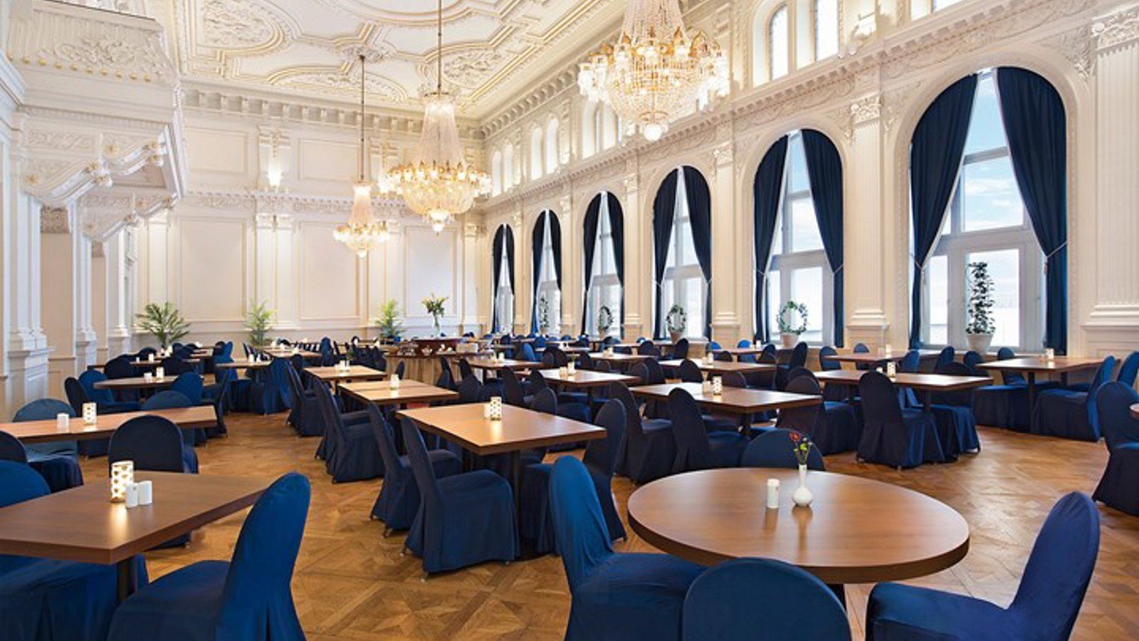 Large room with crystal chandeliers, round tables, white walls and blue details