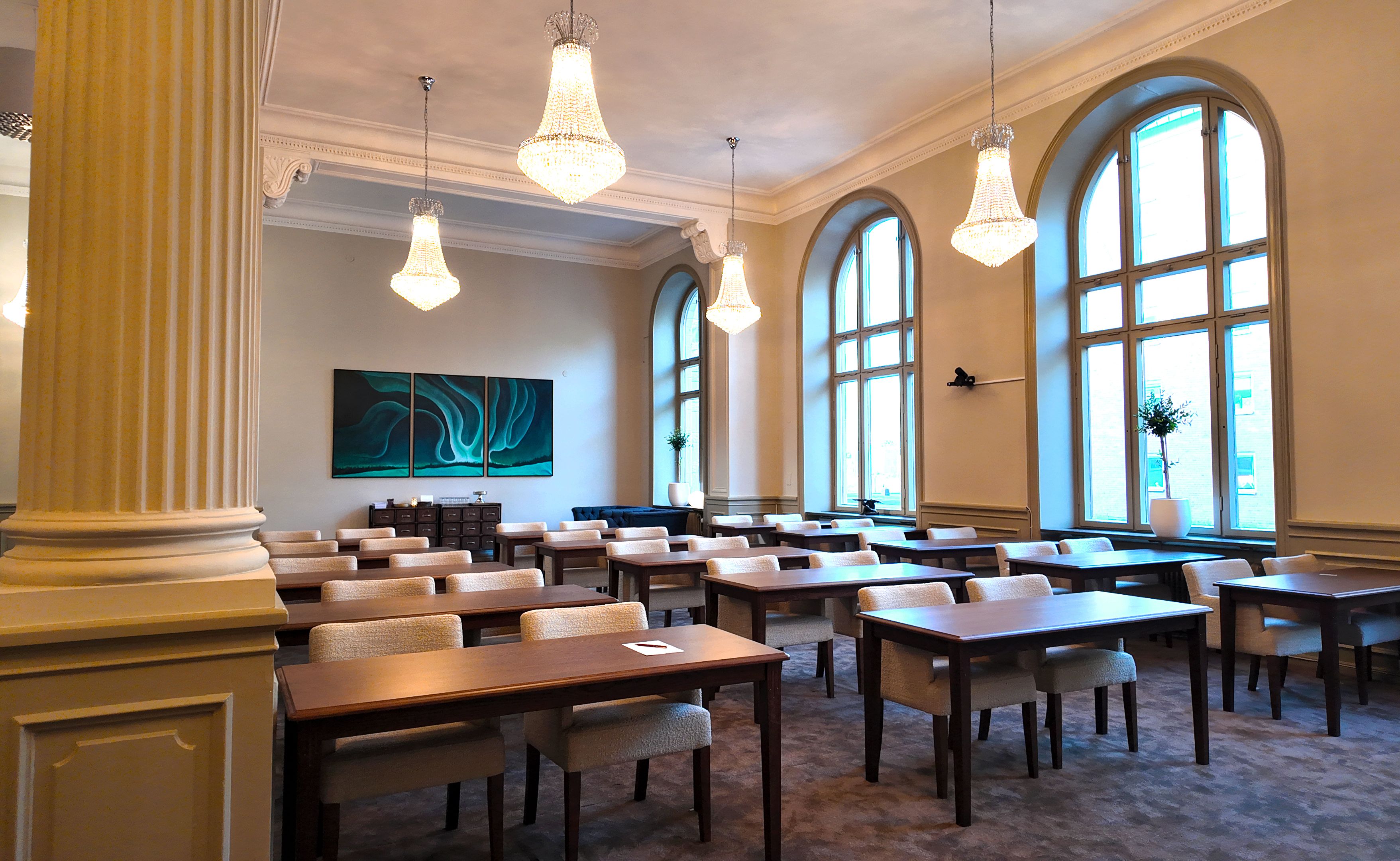 Elegant conference room with chandeliers, large arched windows, and rows of tables and chairs.