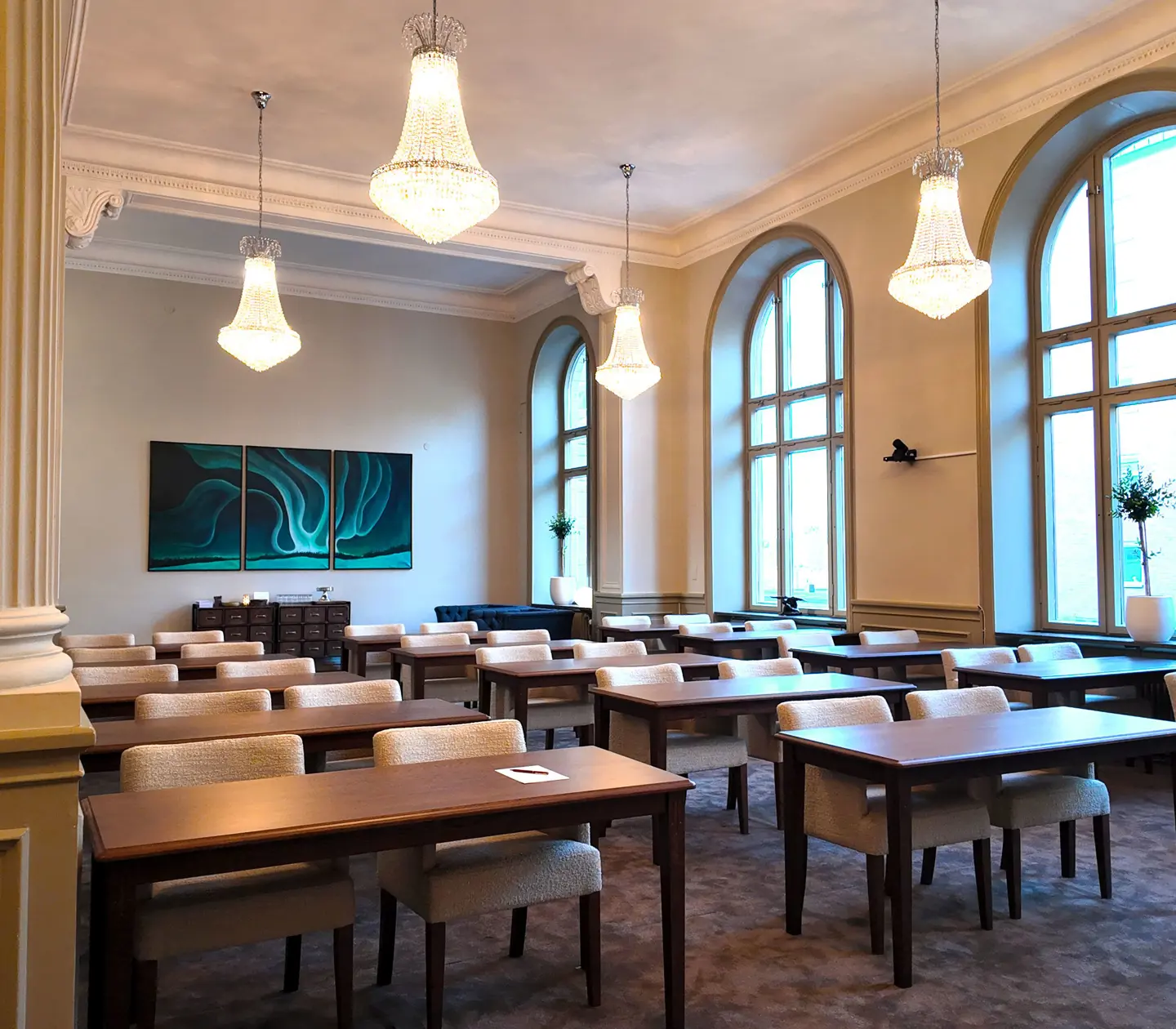 Klassiskt inrett konferensrum med stora fönster, eleganta kristallkronor och stilfulla målningar på väggen, möblerat med träbord och bekväma stolar.