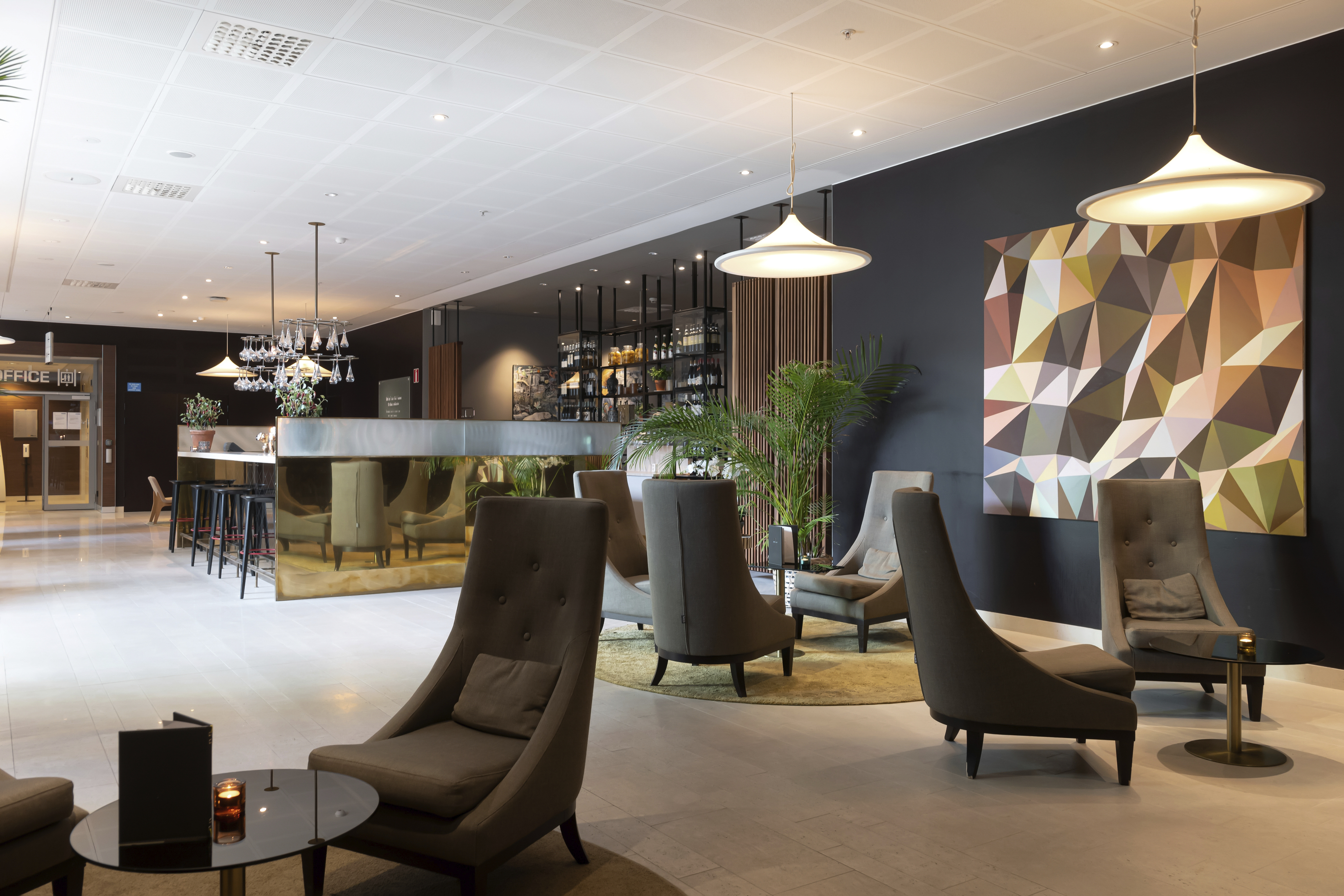 Modern hotel lobby featuring stylish gray furniture, indoor plants, abstract wall art, and elegant lighting, creating a welcoming atmosphere.