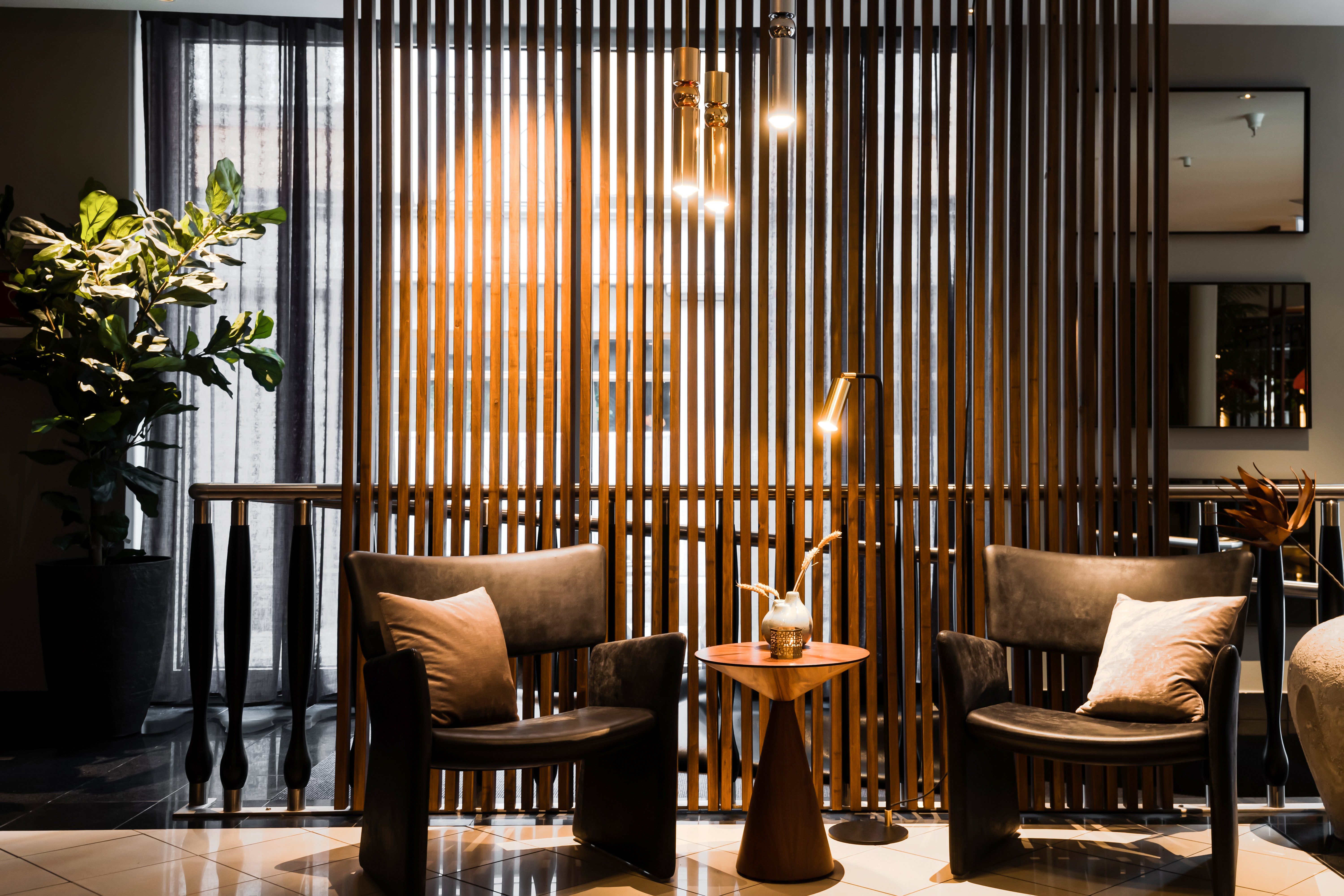 Modern lounge area with two black leather chairs and a small wooden table, surrounded by warm lighting and vertical wooden slats.