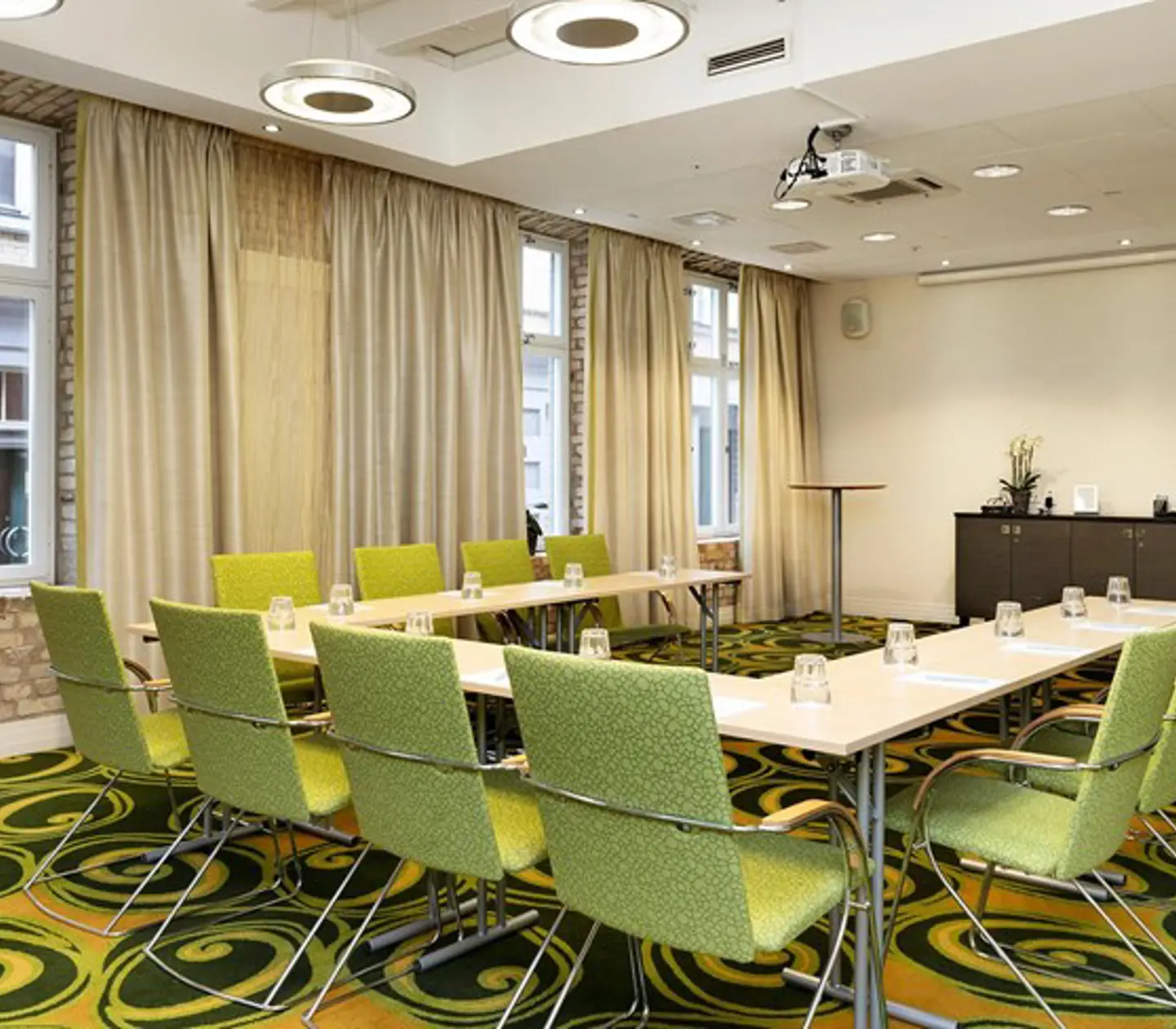 Konferensrum med u-sittning, gröna stolar, grönmönstrad matta och stora fönster