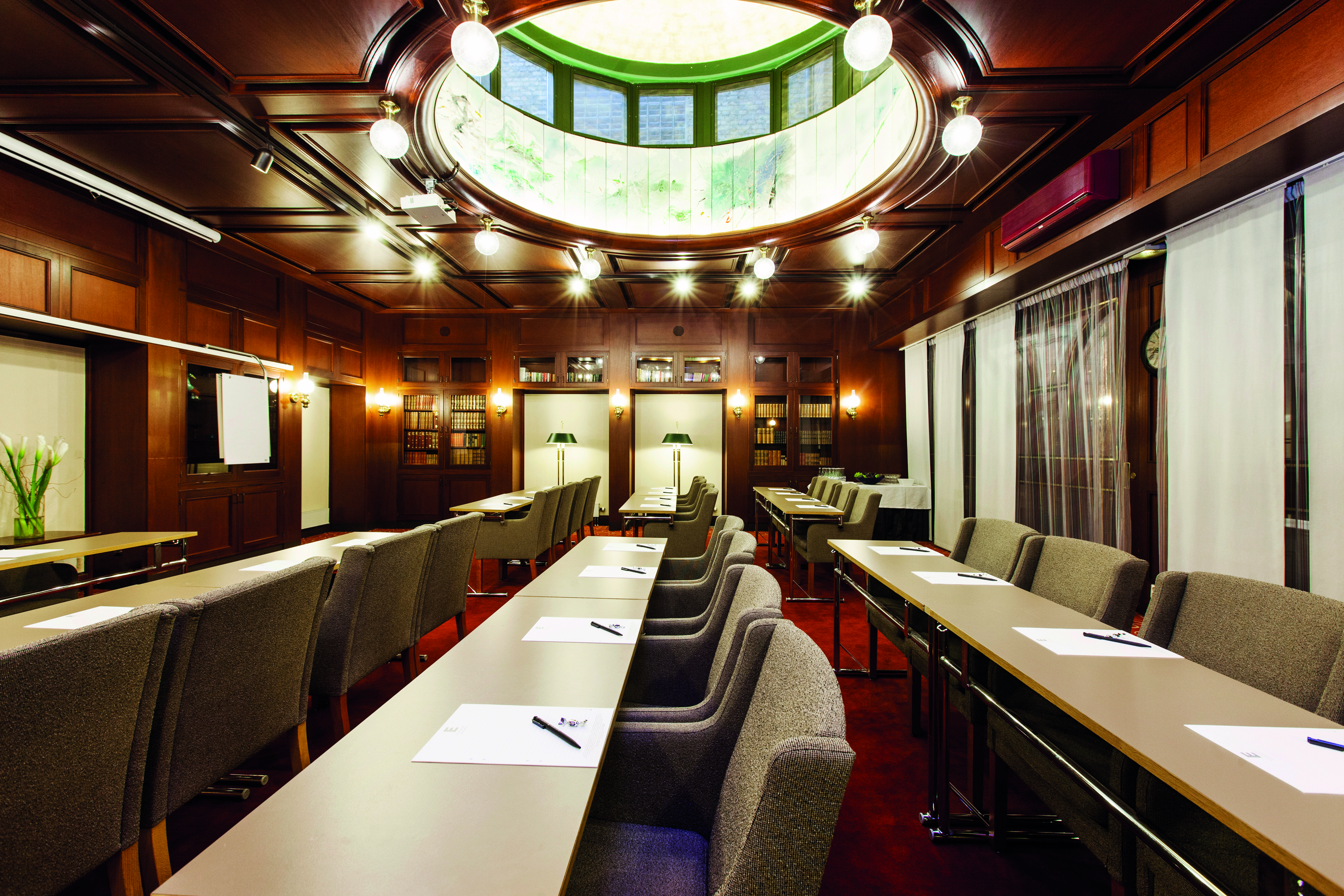 Konferensrum med elegant träinredning, stora fönster, omslutande takfönster och uppställda bord och stolar för möten.