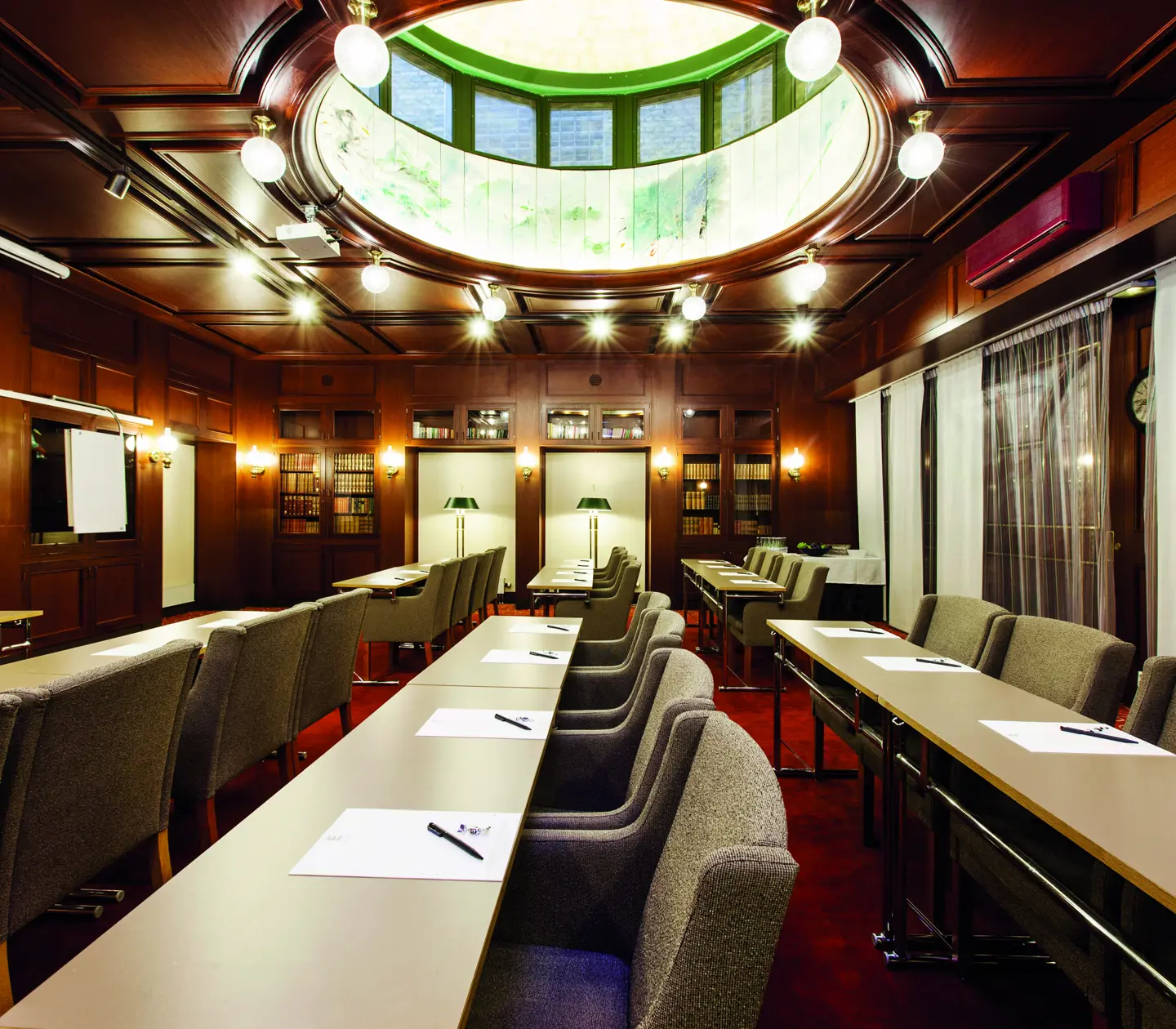 Konferensrum med elegant träinredning, stora fönster, omslutande takfönster och uppställda bord och stolar för möten.