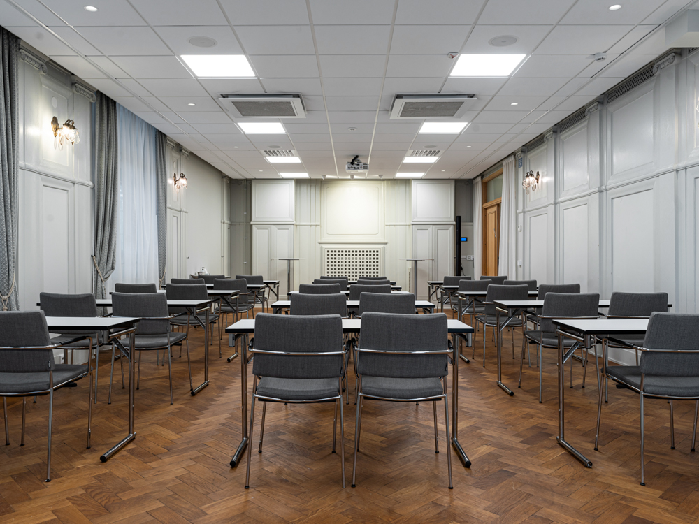 Konferensrum med uppställda stolar och bord, trägolv och vita väggar, redo för möte.