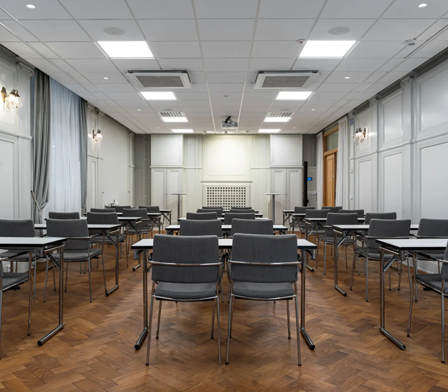 Konferensrum med uppställda stolar och bord, trägolv och vita väggar, redo för möte.