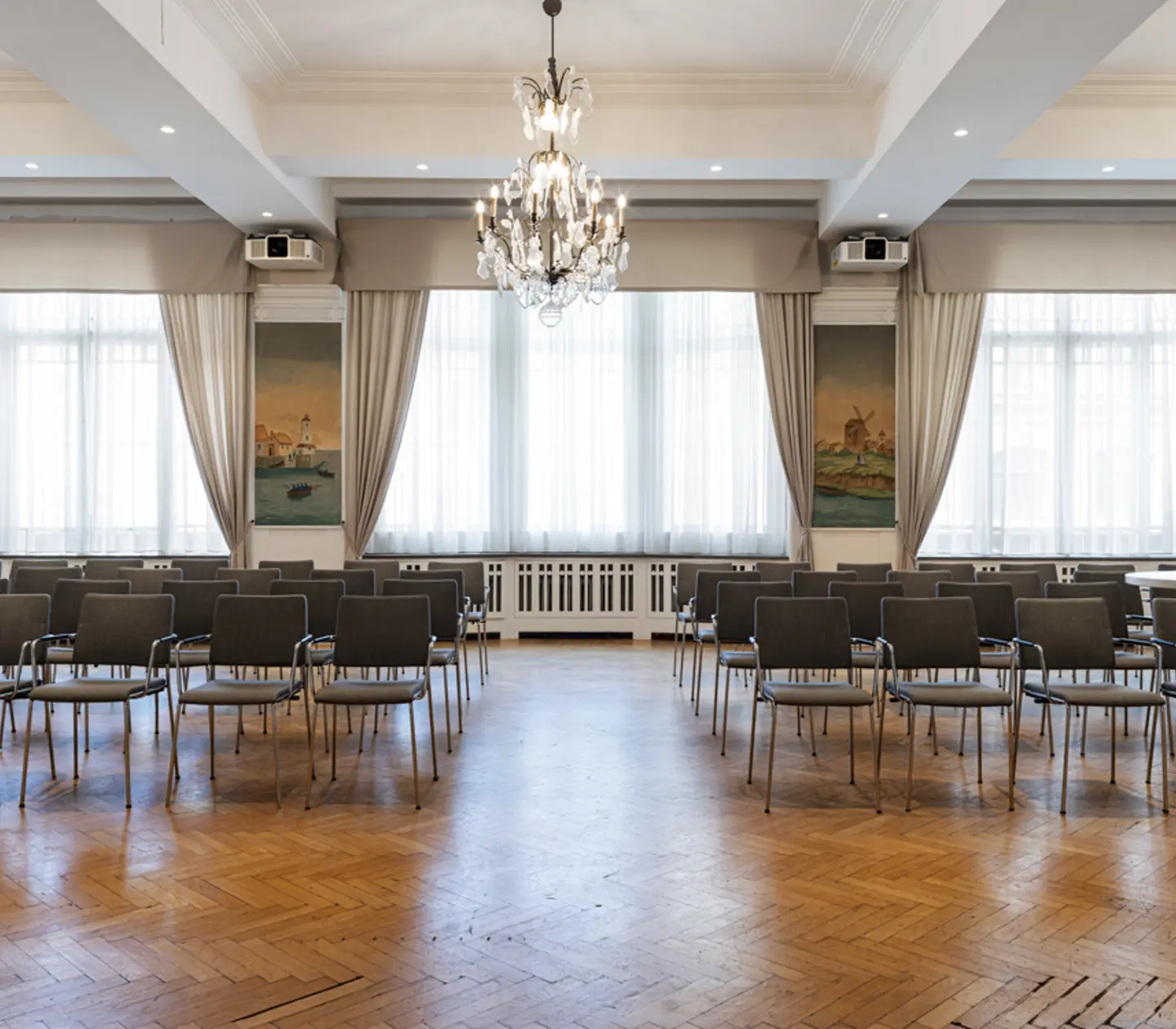 Ljus konferenssal med stolsuppställning, parkettgolv, och elegant kristallkrona.