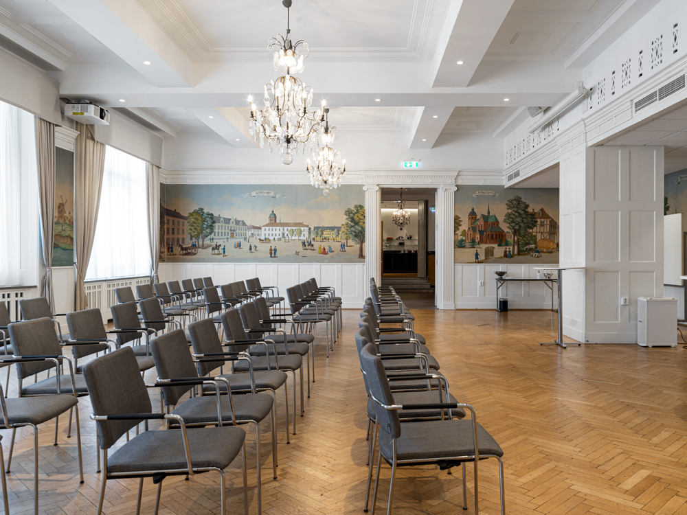 Konferensrum med stolsrader, parkettgolv och målade väggpaneler.