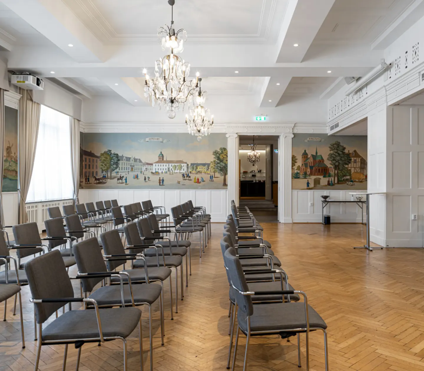 Konferensrum med stolsrader, parkettgolv och målade väggpaneler.