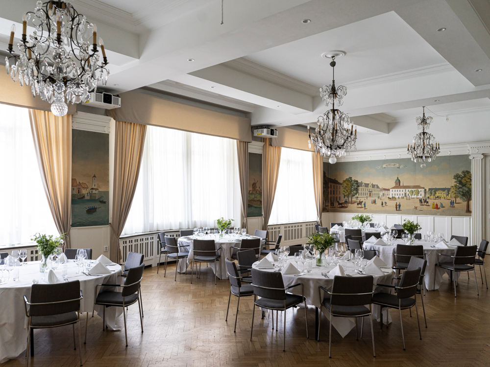 Elegant matsal med ljuskronor och dukade runda bord inredd i klassisk stil, perfekt för bröllop eller festliga tillställningar.