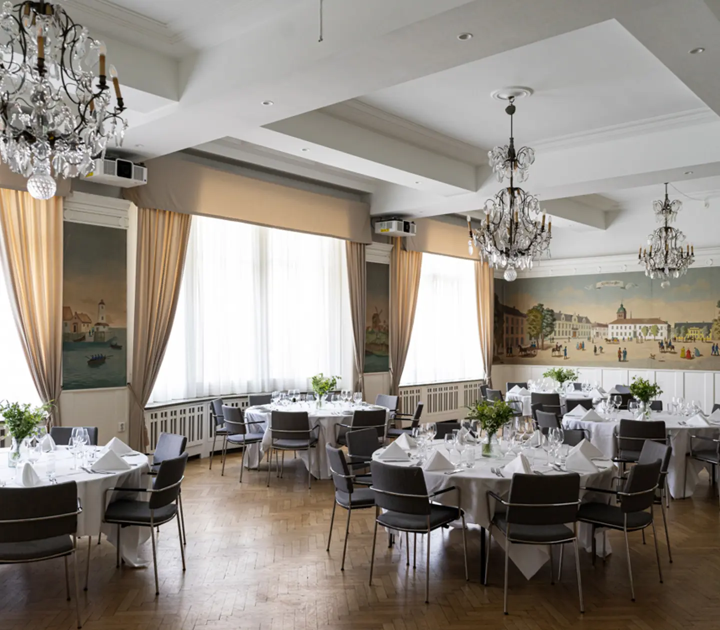 Elegant matsal med ljuskronor och dukade runda bord inredd i klassisk stil, perfekt för bröllop eller festliga tillställningar.