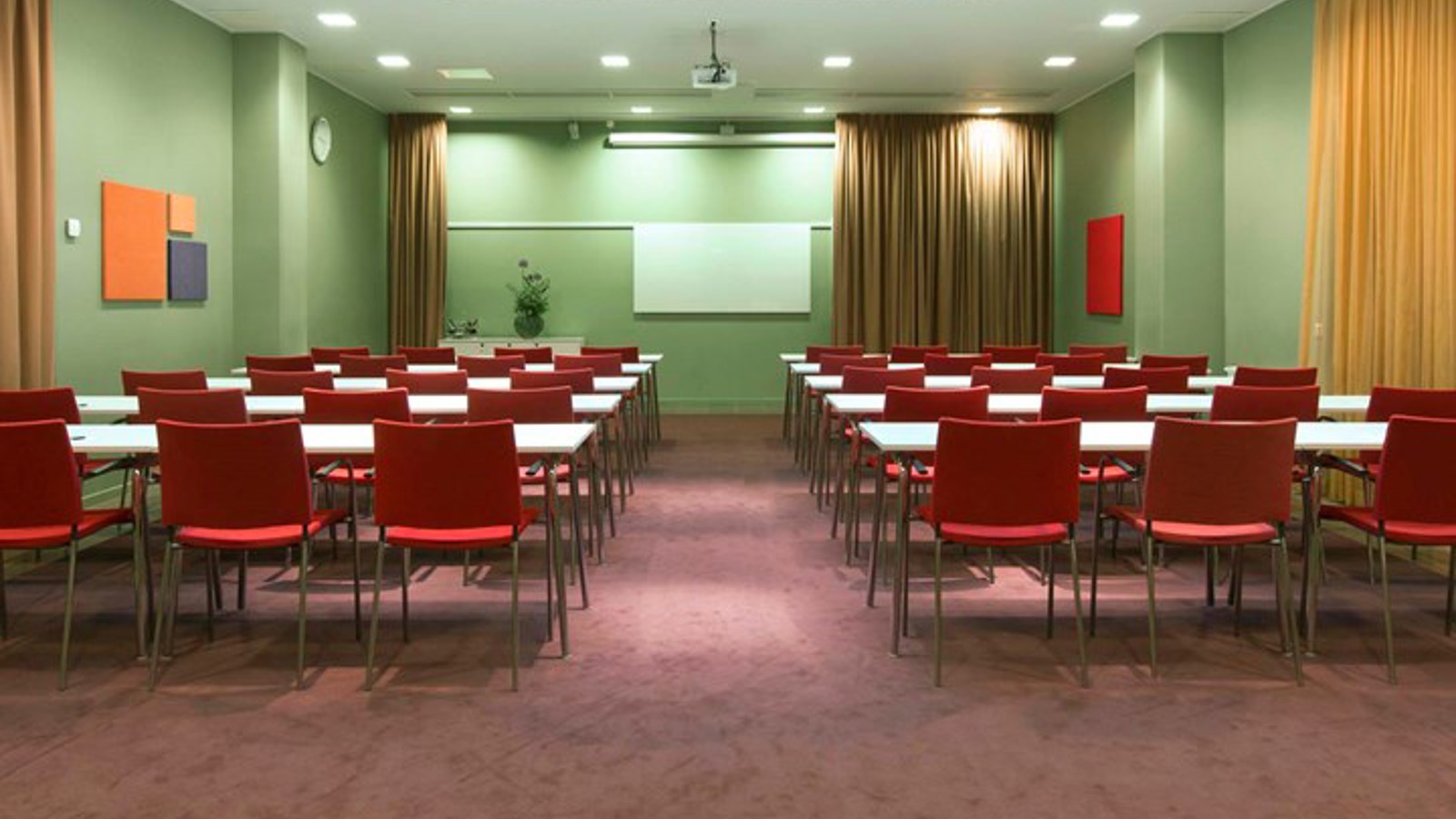 Conference room with lined up red chairs, green walls and yellow draperies