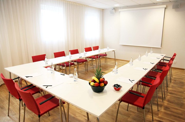 Conference room with u-shaped seating, white walls, white table and red chairs