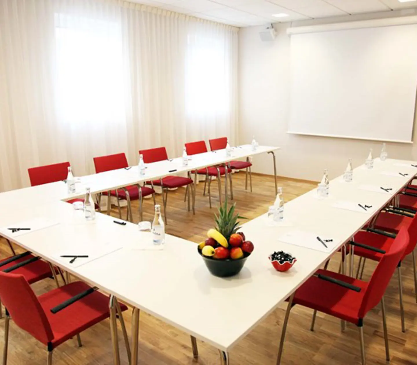 Konferensrum med u-sittning, vita väggar, vitt bord och röda stolar