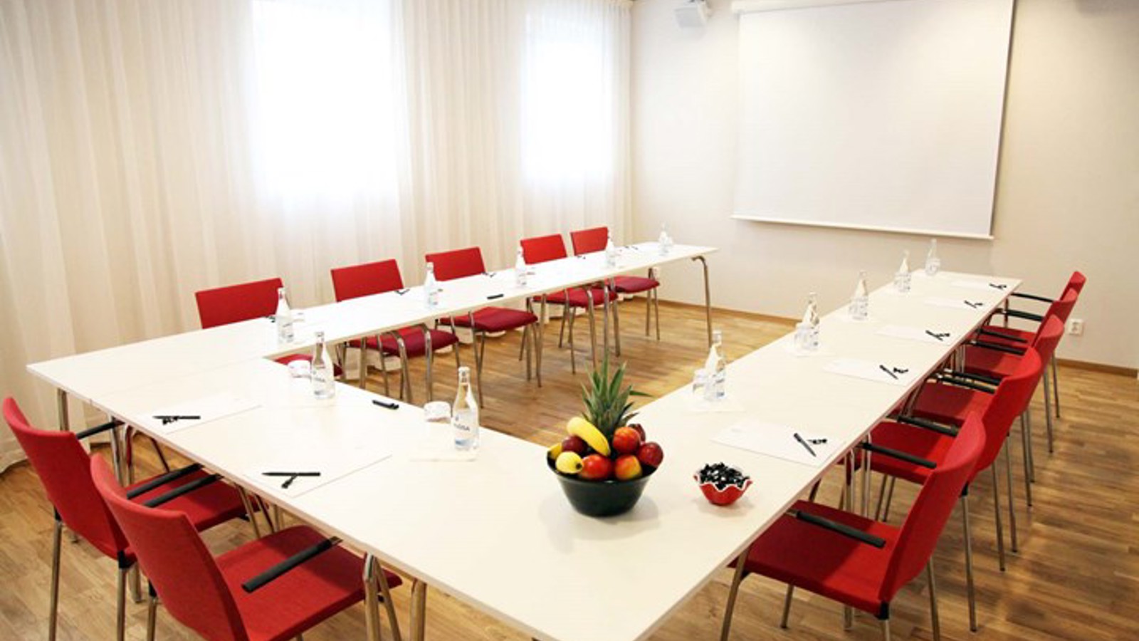 Conference room with u-shaped seating, white walls, white table and red chairs