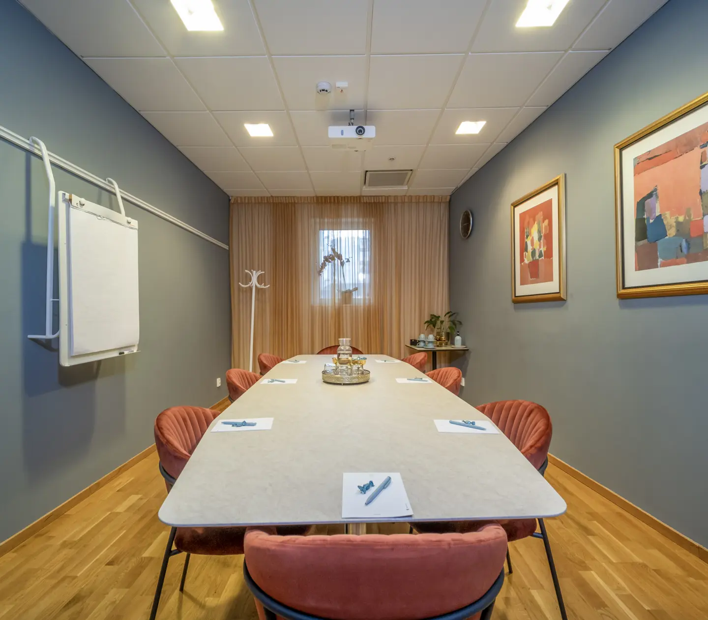 Konferensrum med styrelsesittning, vitt bord, röda stolar och vita väggar