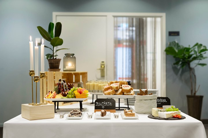 Image of buffet table with white tablecloth, coffee, fruit, cheeses and lighted candles
