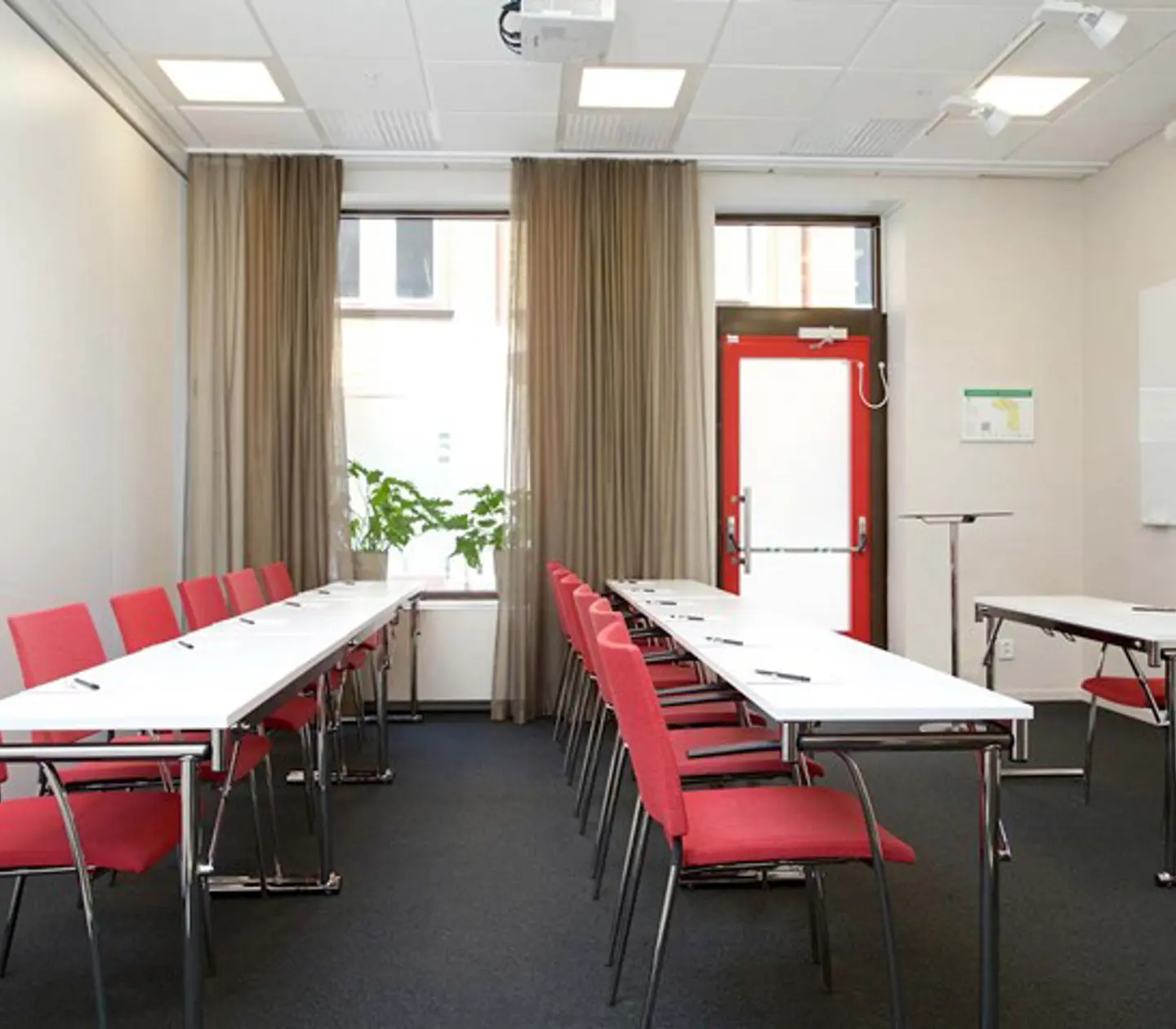 Konferensrum med skolsittning, vita bord, röda stolar och stort fönster