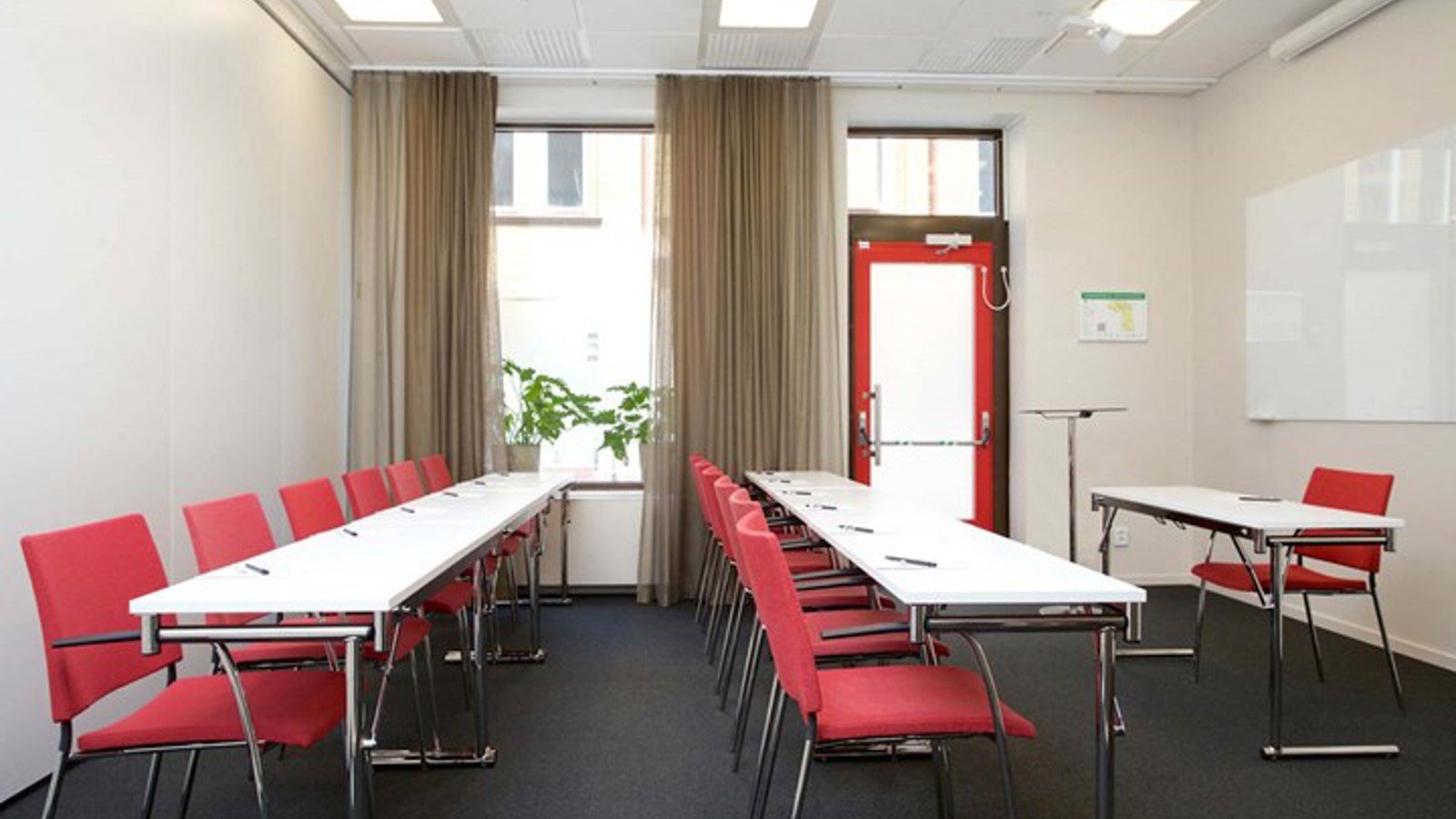 Conference room with lined up chairs, white tables, red chairs and large window