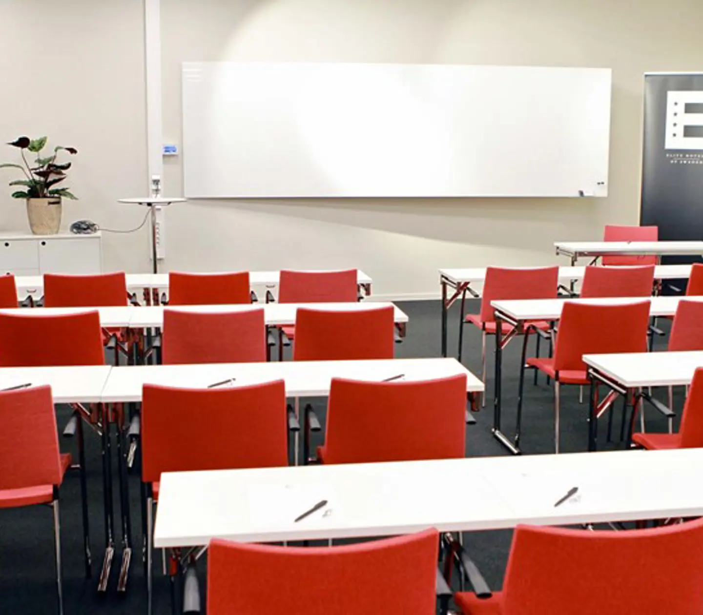 Konferensrum med skolsittning, vita bord, röda stolar