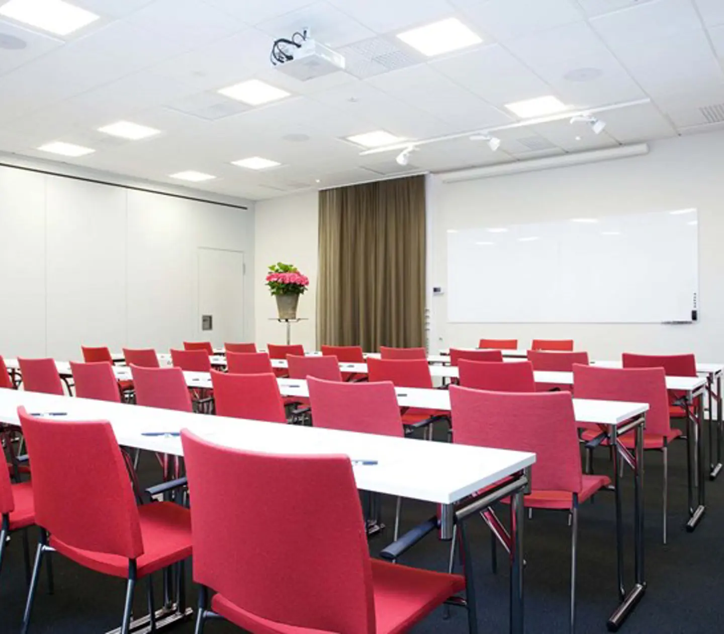 Konferensrum med vita bord, röda stolar, svart golv
