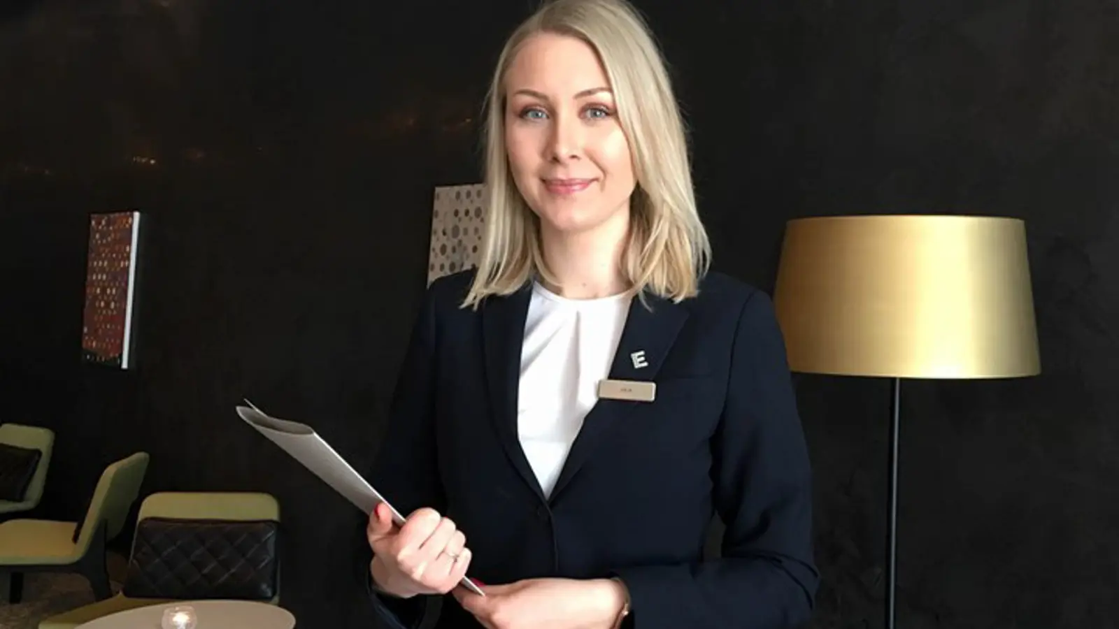 Närbild på hotellpersonal med broschyr i handen, mörk vägg bakom
