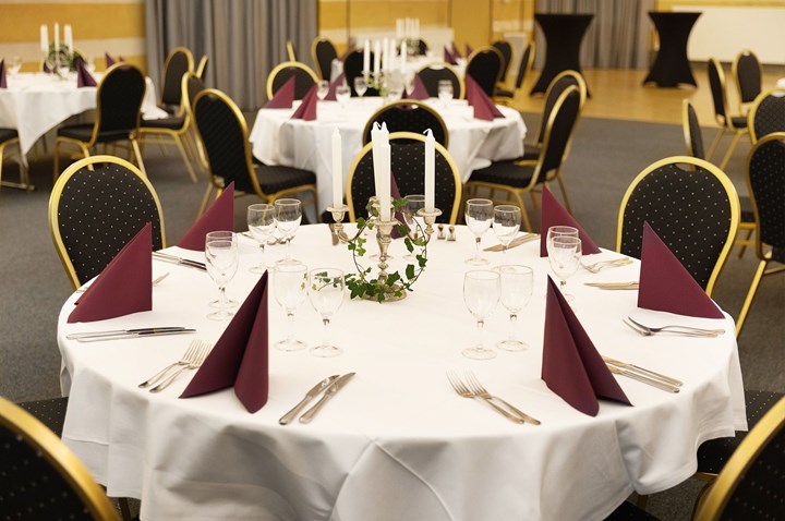 Room with round tables, white tablecloths, glasses and candles