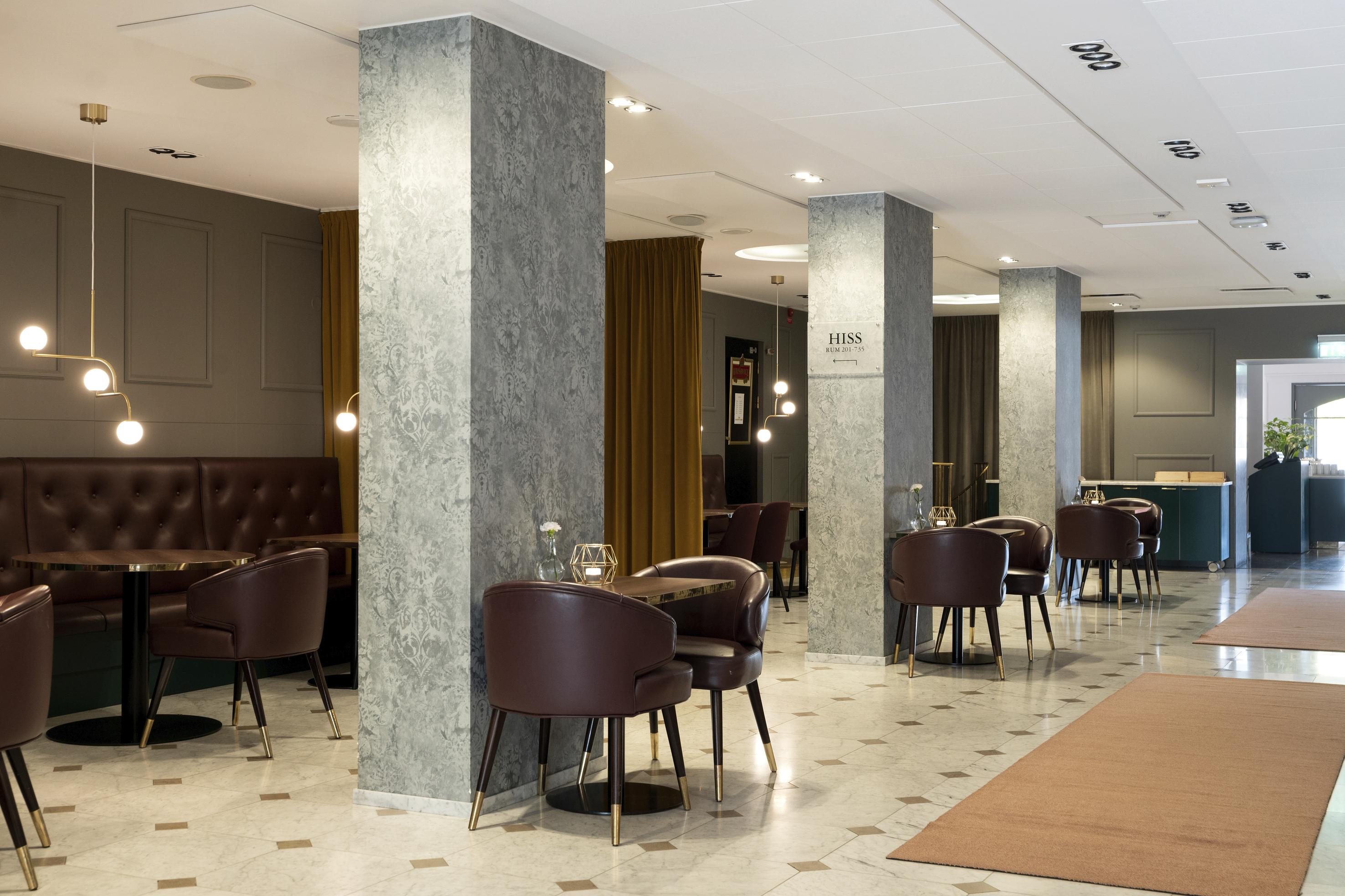 Modern hotel lobby with stylish marble pillars, brown leather chairs, and elegant lighting.