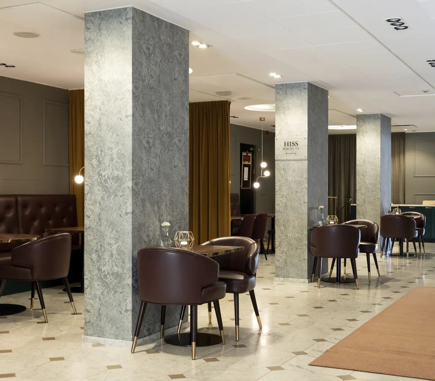 Modern hotel lobby with stylish marble pillars, brown leather chairs, and elegant lighting.