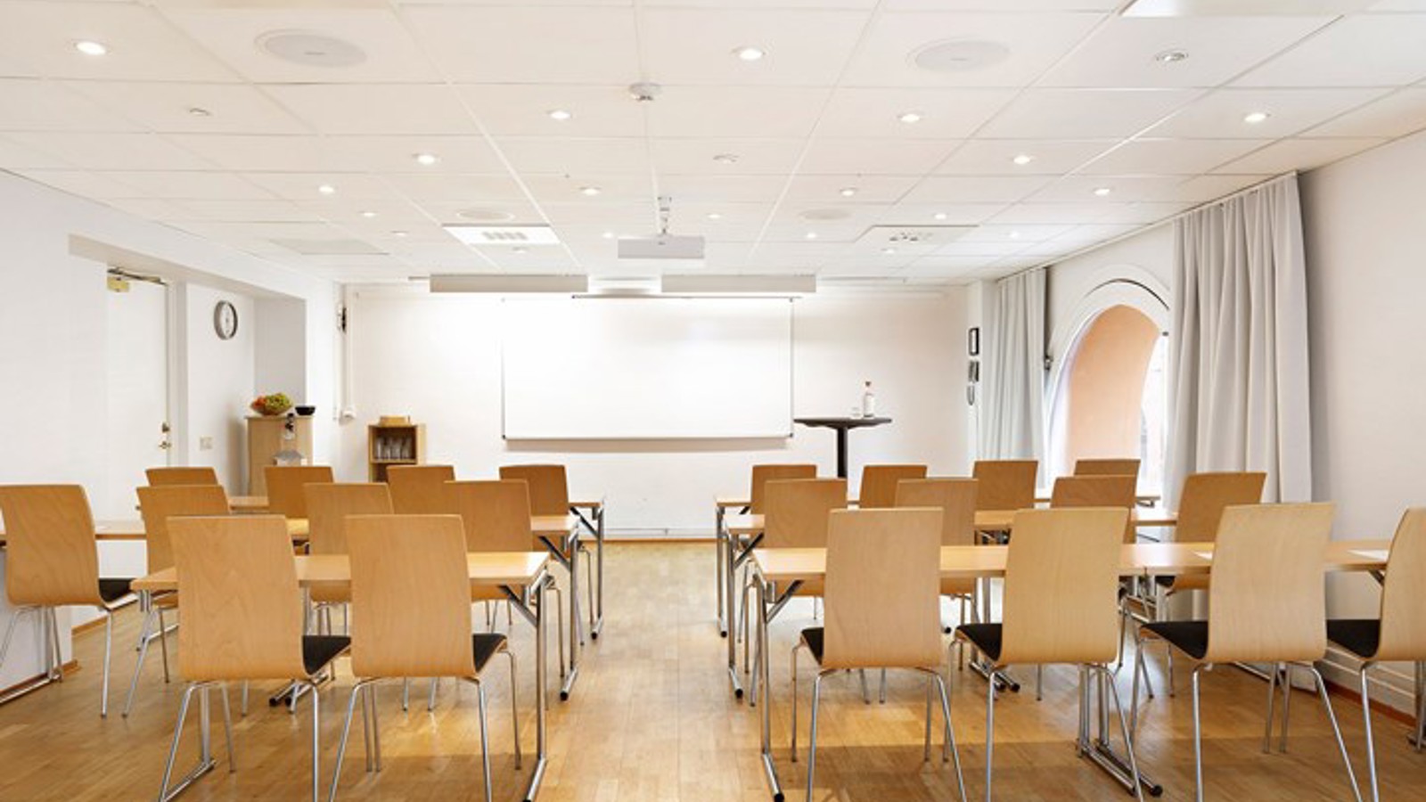 Bright conference room with school seating, white walls and wooden floor