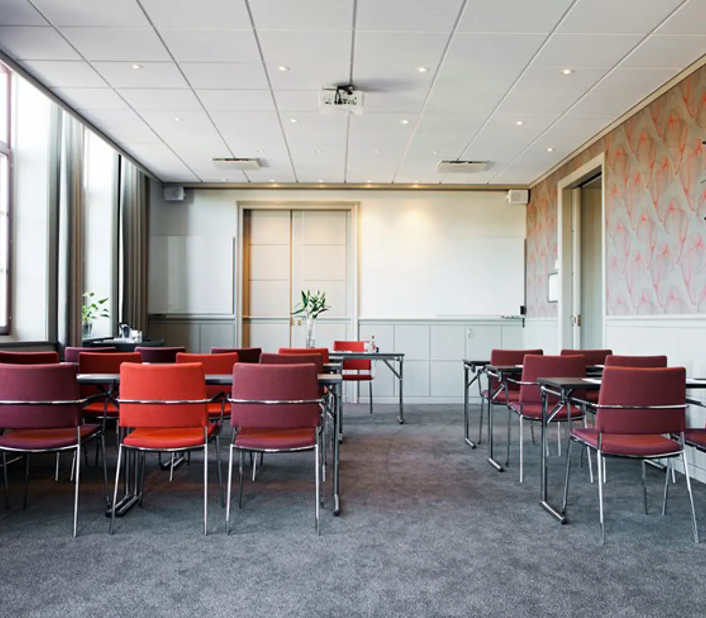 Konferensrum med skolsittning, grå matta, röda stolar, stora fönster