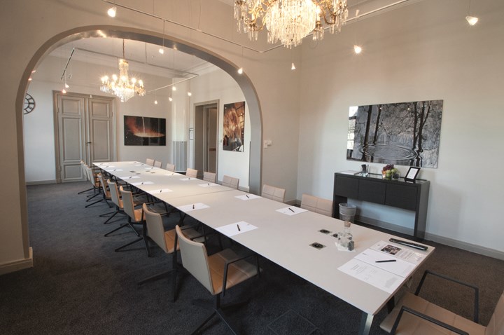 Konferenslokal med styrelsesittning, vita väggar, kristallkronor och valv