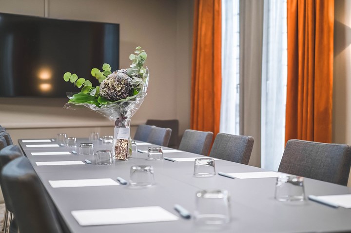 Konferensrum med styrelsesittning, grått bord, grå stolar, rostbruna gardiner