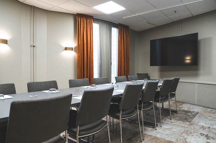 Konferensrum med styrelsesittning, grå stolar, grått bord, tv, rostbruna gardiner