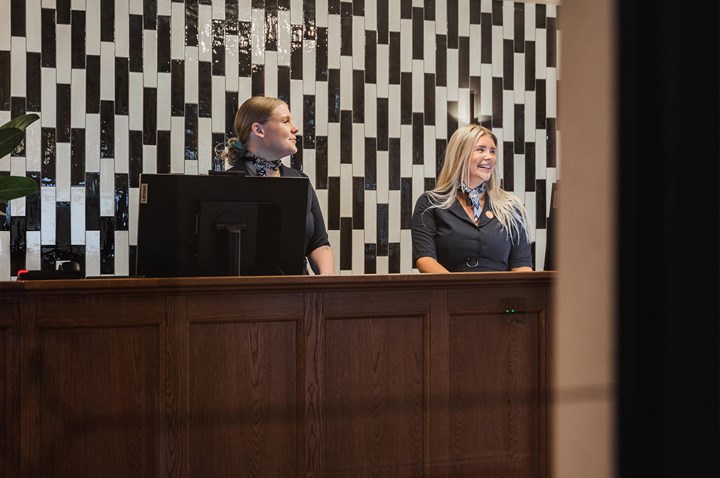 Reception i brunt trä med personal, vit och svart-mönstrad vägg bakom