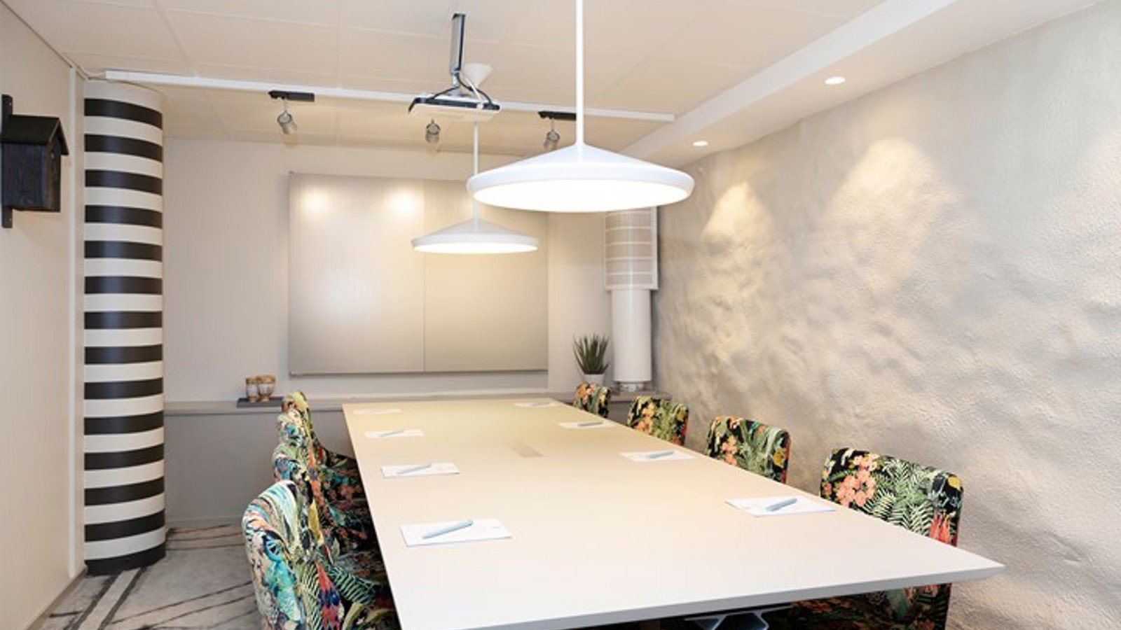 Conference room with board seating, white table, white walls and patterned chairs