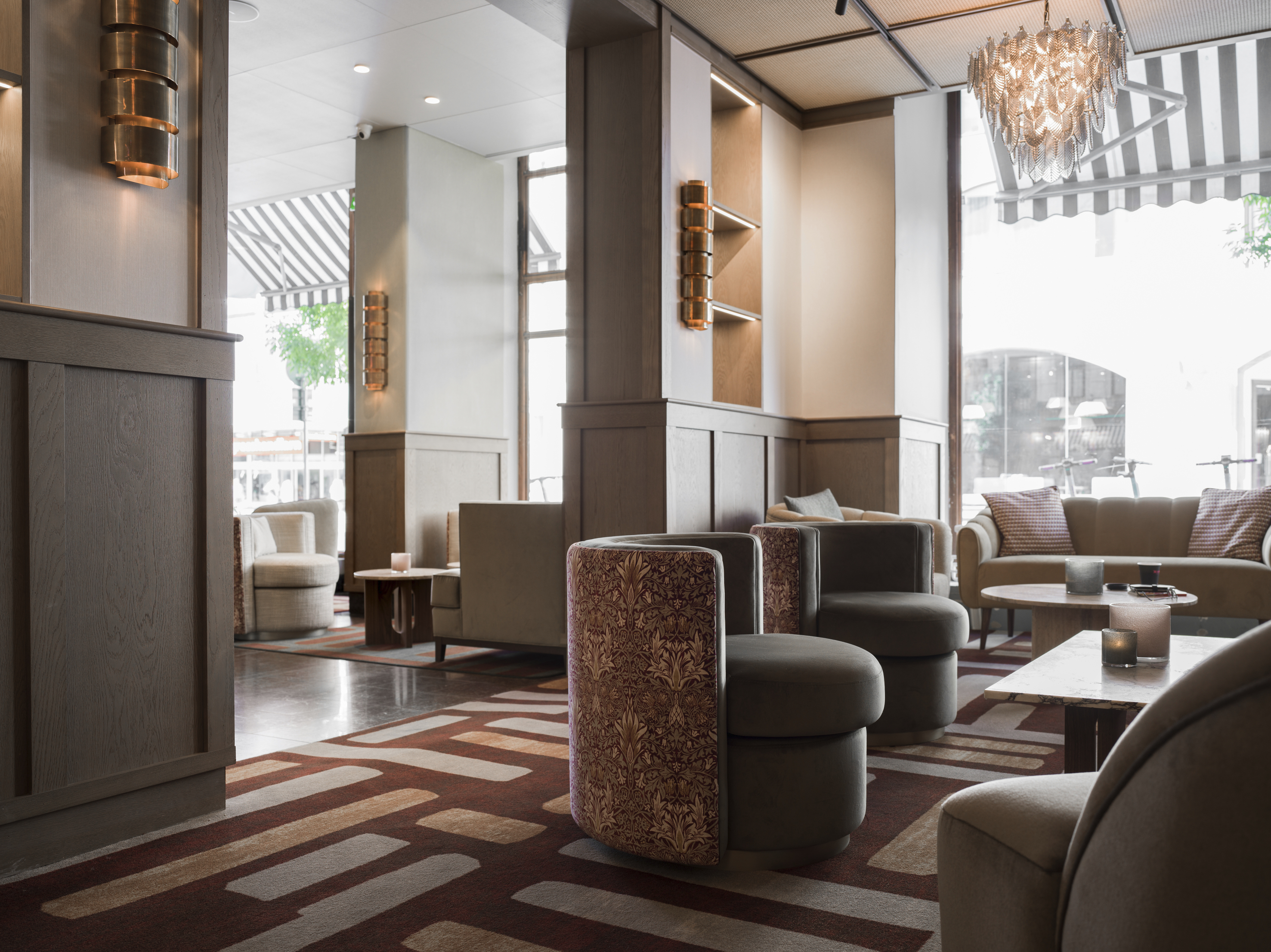 Modern och elegant hotellobby med stilfull inredning, inklusive bekväma fåtöljer och soffor, ett stort fönster som släpper in naturligt ljus och en glamorös ljuskrona.
