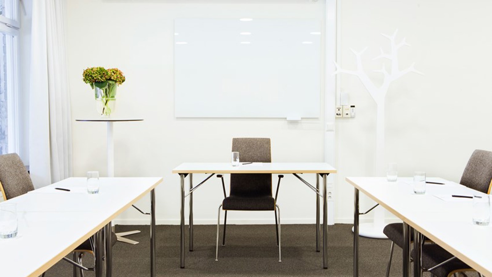 Conference room with u-shaped seating, white tables, white walls and gray carpet