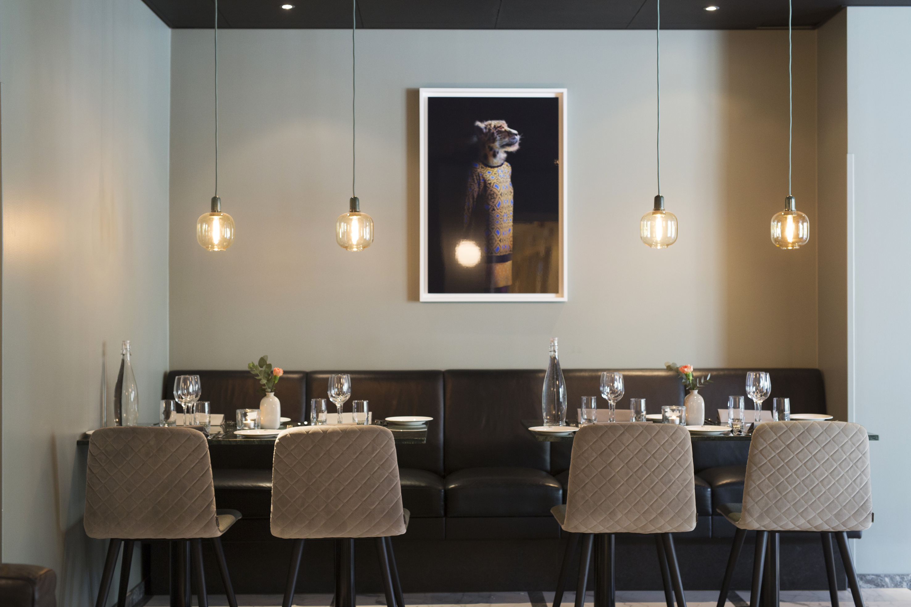 Modern restauranginteriör med fyra stolar vid ett dukat bord, hängande lampor och en tavla på väggen.