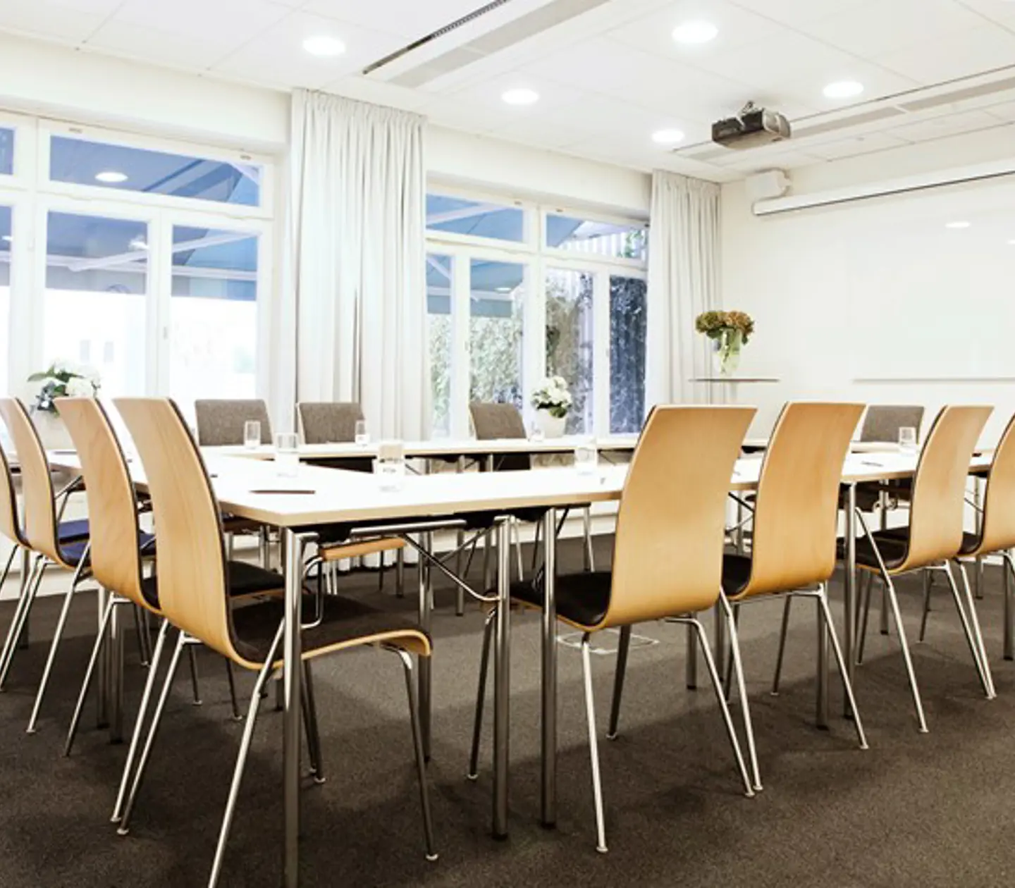 Konferensrum med u-sittning, vita väggar, stora fönster, grå matta