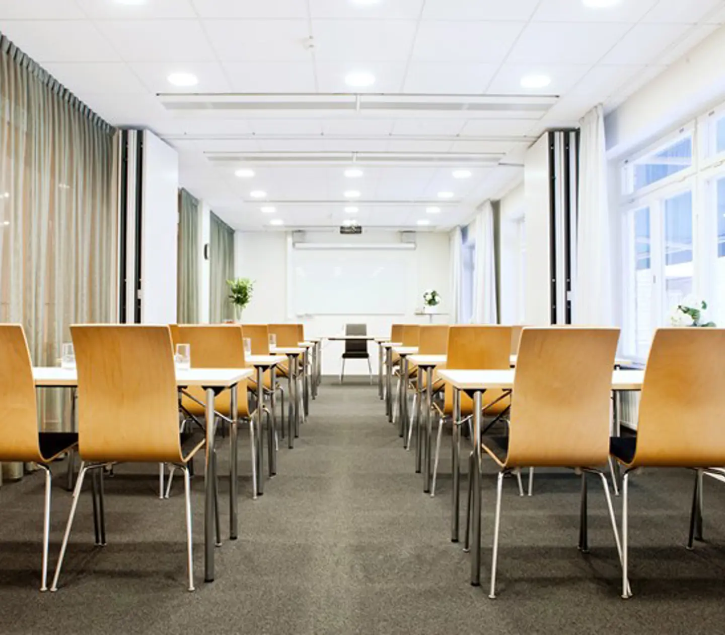 Konferensrum med skolsittning, trästolar, vita väggar, stora fönster