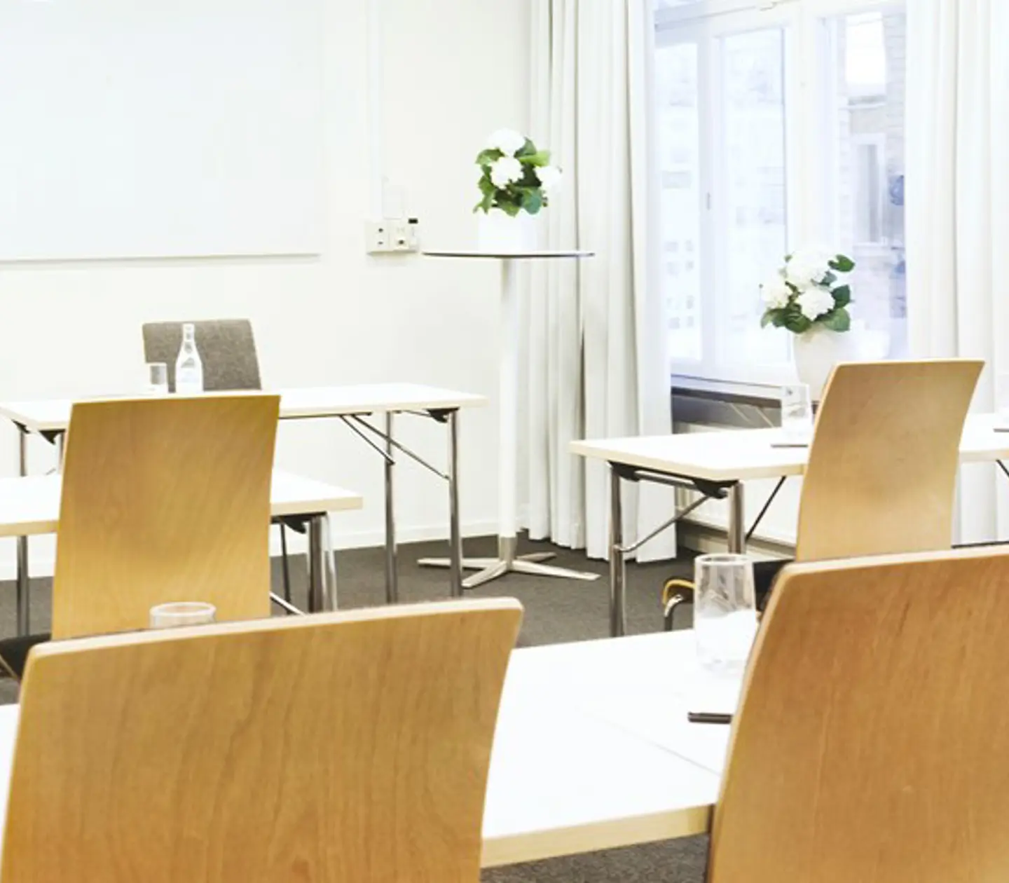 Konferensrum med skolsittning, trästolar och vita väggar