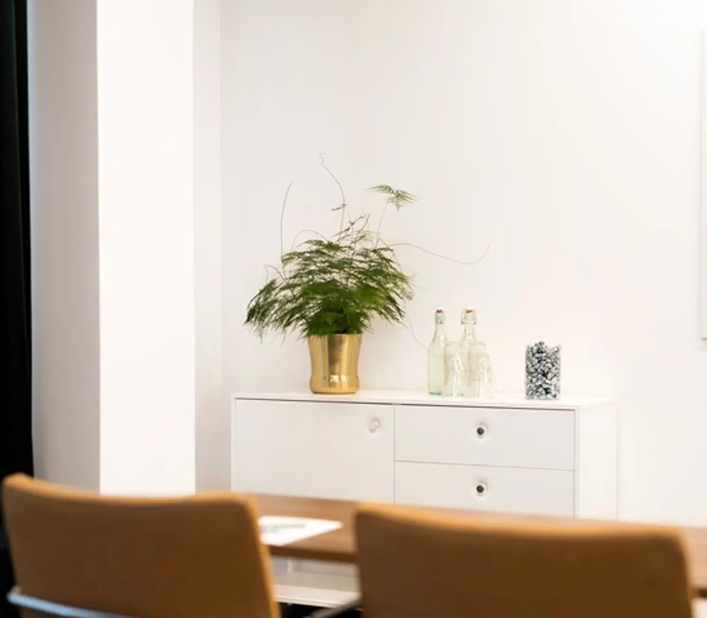 Detaljbild från konferensmiljö, med stolsryggar i förgrunden och vit vägg med byrå i bakgrunden