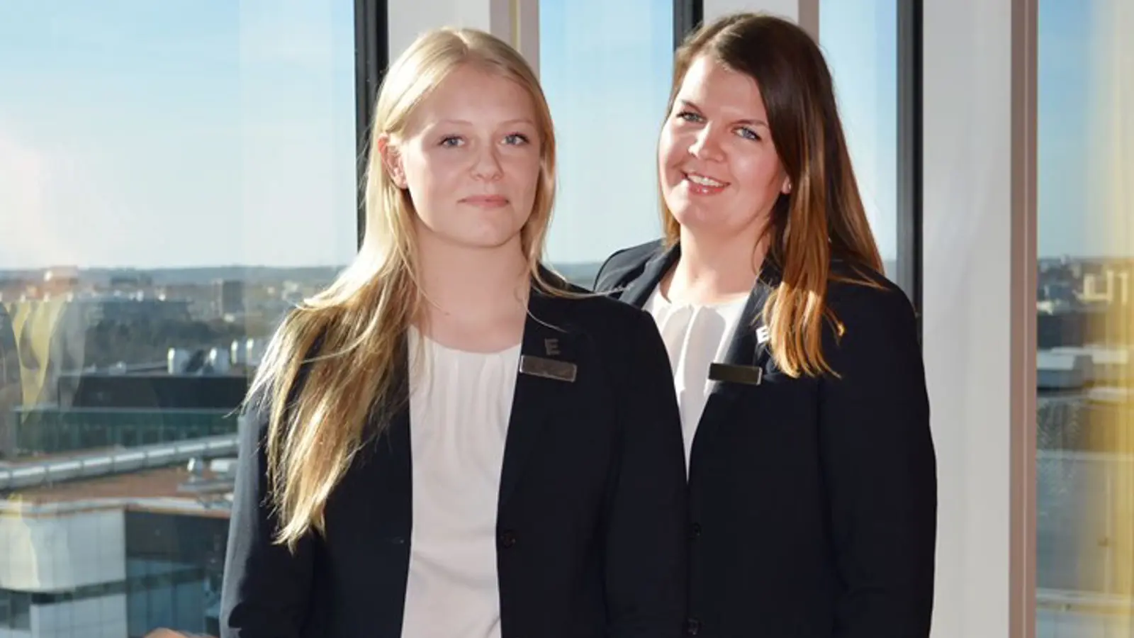 Porträtt på två personer, stående vid stort fönster med utsikt